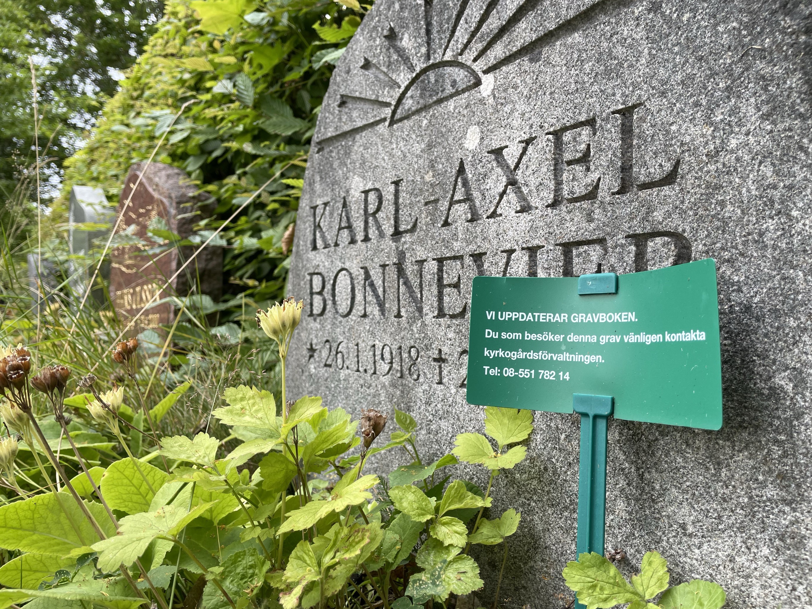 Gravplats med grön skylt. På gravplatsen finns en grå gravsten med texten "Karl-Axel Bonnevier".