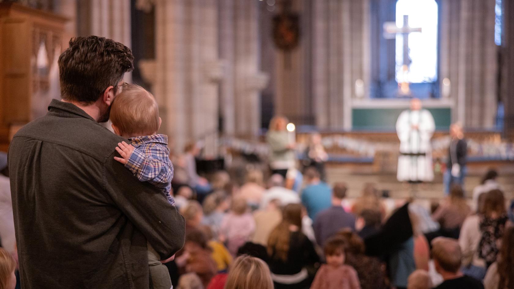 Barnmässa i Uppsala domkyrka. En pappa håller sitt lilla barn i famnen medan de blickar mot prästen som står vid altaret.