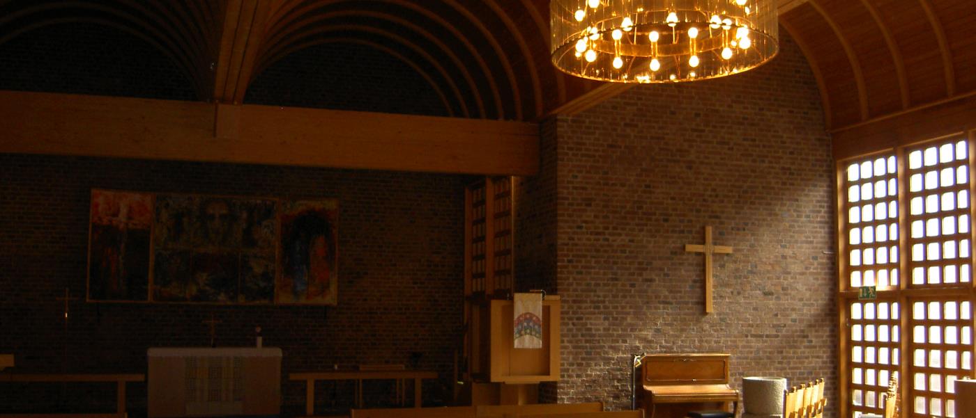 Interiörbild från Almtunakyrkans kyrkorum med dagsljus från höger som dfaller över inredningen och ett väggkors i trä.