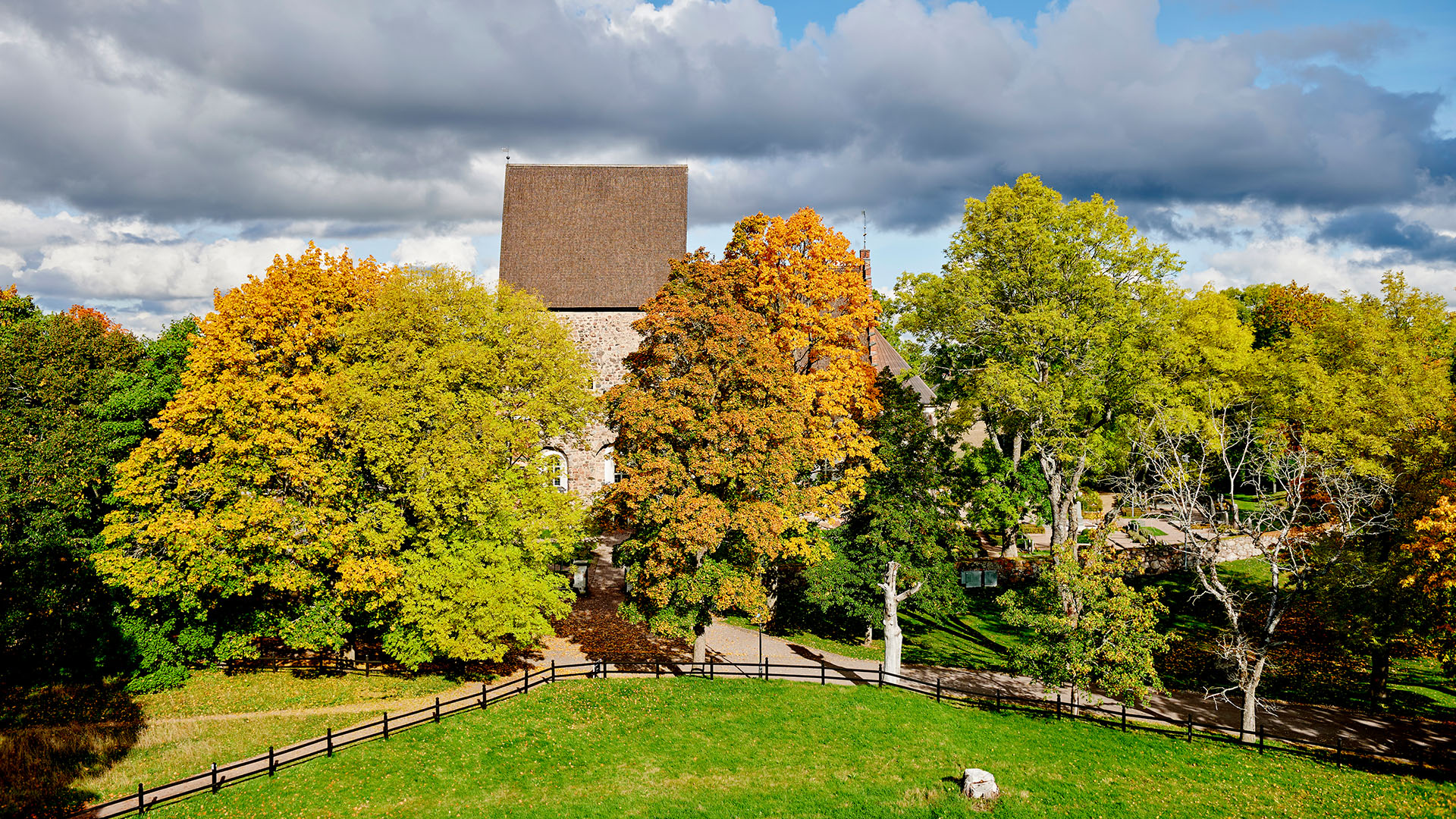 Landskap med ett kyrktorn i bakgrunden och träd i skiftande höstfärger i förgrunden.