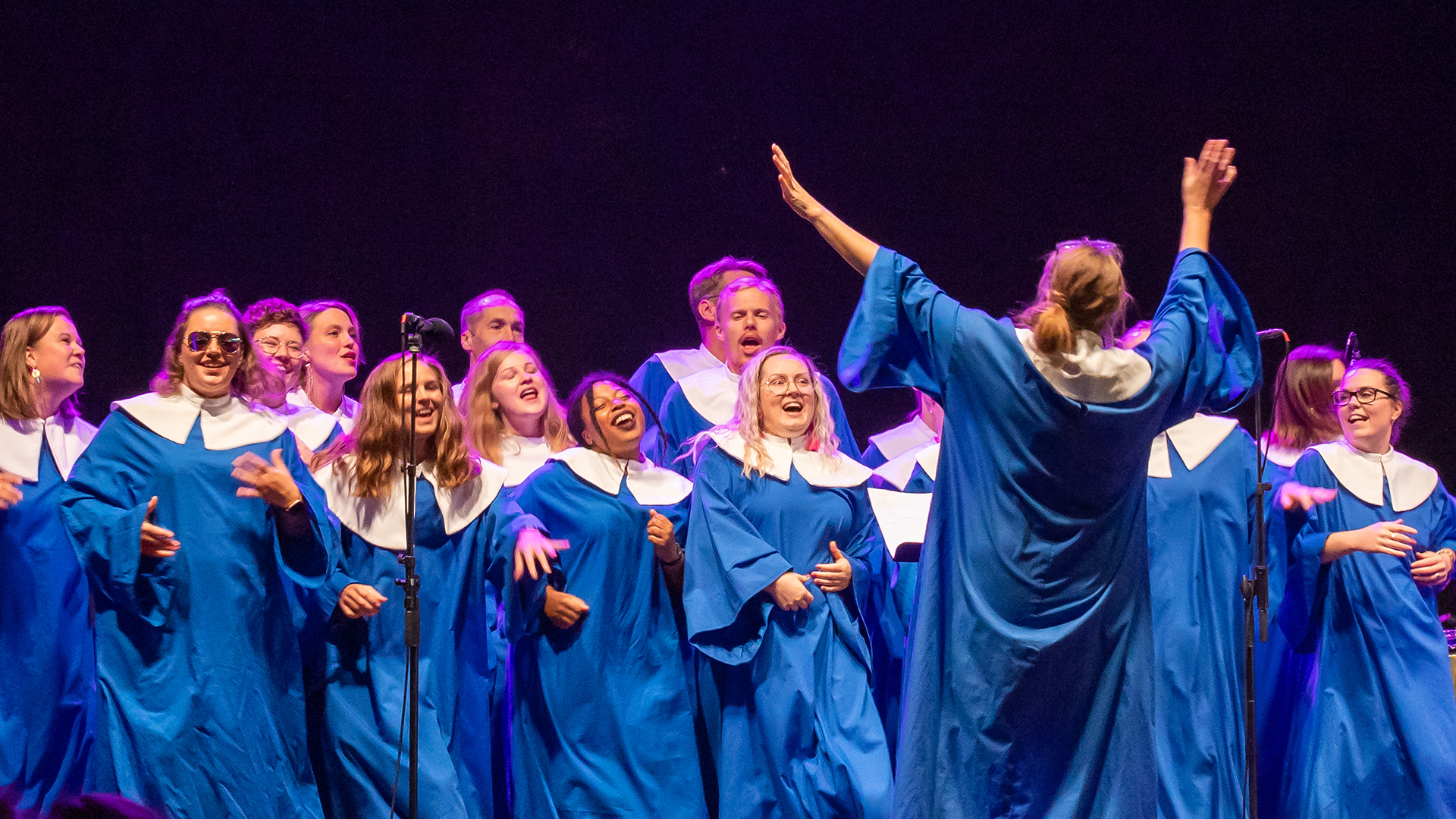 Kören Gloryfires sjunger och dansar i blå kåpor och med gott humör, uttrycksfullt dirigerade av sin körledare Johanna Engholm.