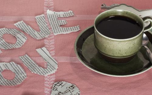En kopp svart kaffe står på en rosa bordduk där någon också har klippt ut bokstäver som bildar ord samt ett hjärta med noter i.