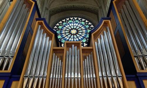 Ruiffatiorgelns orgelverk syns i förgrunden och uppe på norra korväggen bakom orgeln skymtar Andens fönster med en duva i mitten av rosettkompositionen.