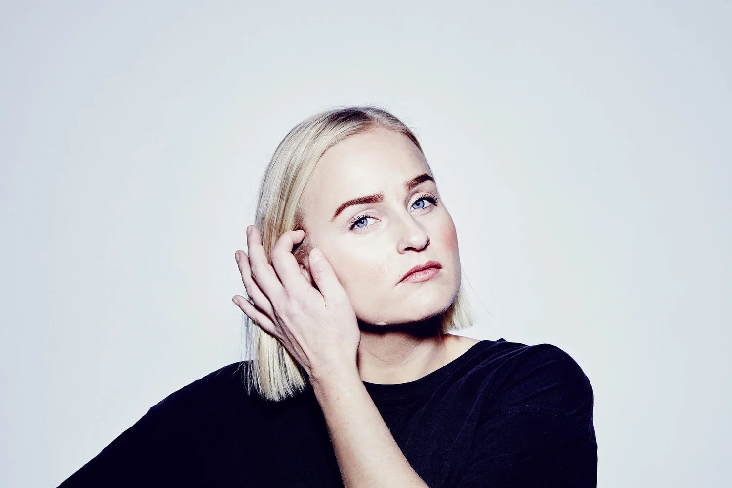 Lovisa Jennervall, i blond pagefrisyr och svart tröja, rättar till håret bakom högra örat och blickar in i kameran med allvarlig uppsyn.