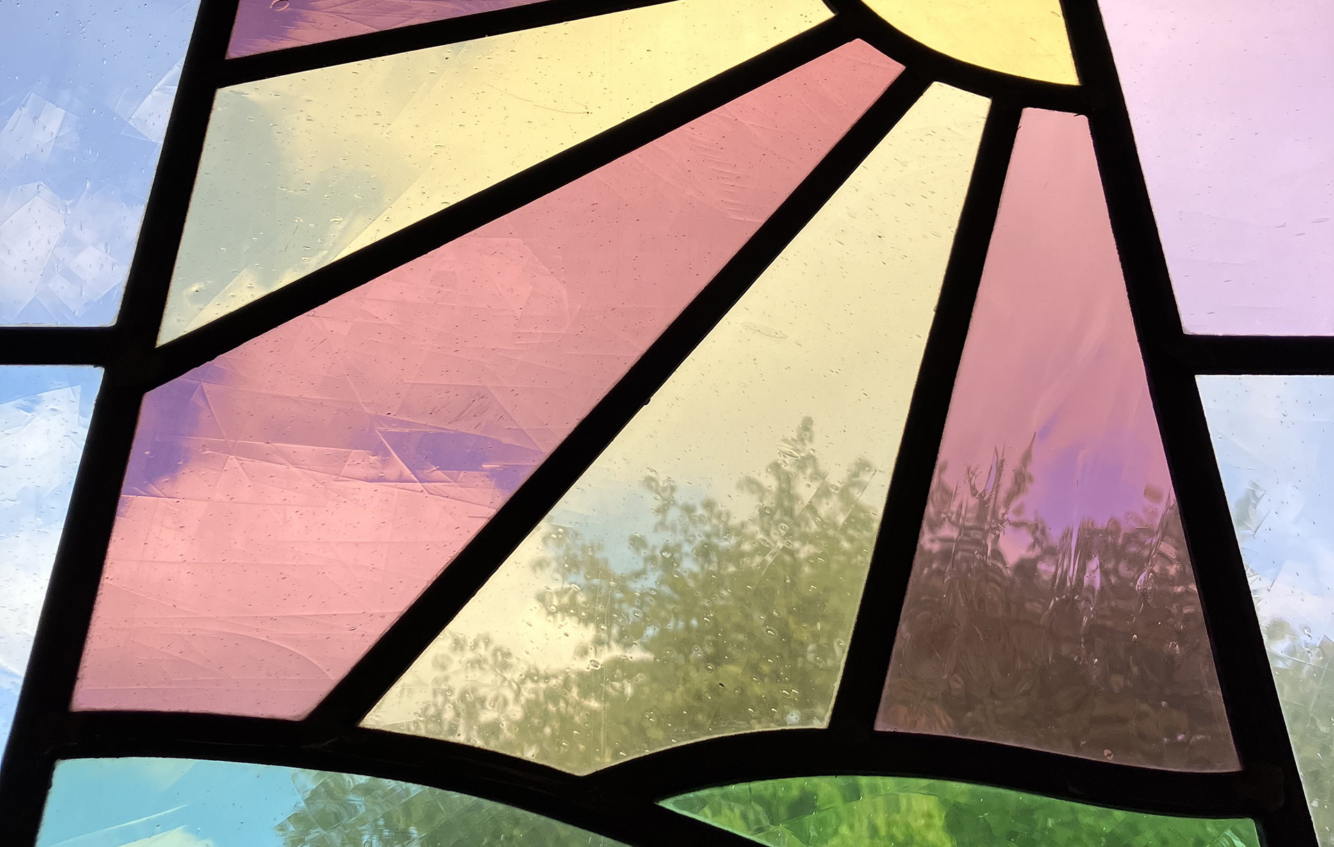 Ett av Vindhemskyrkans glasfönster med motivet sol över gröna kullar.