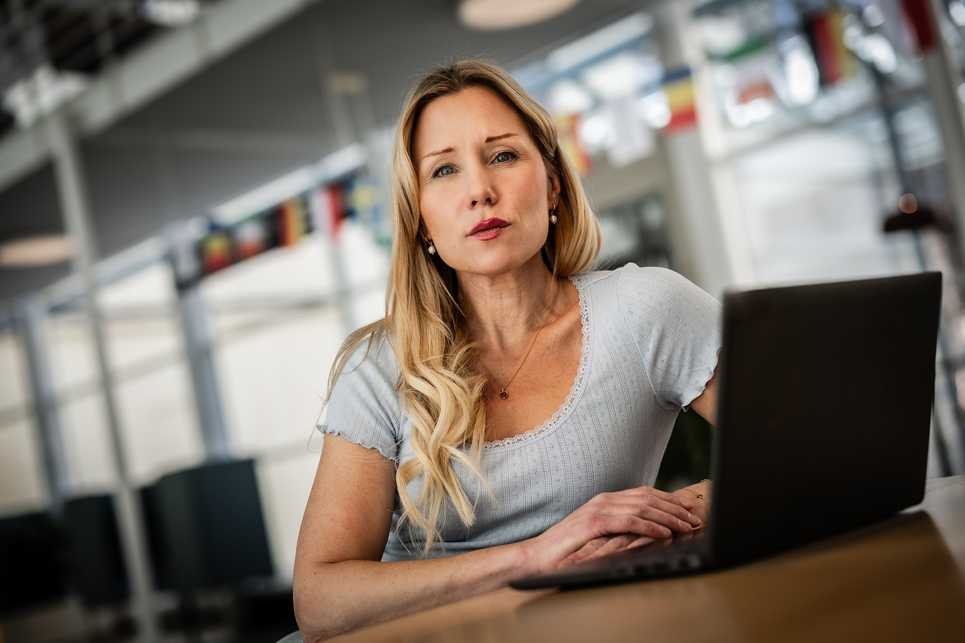 Sara Skoog Waller sitter vid sin laptop i ljus och luftig kontorsmiljö och ser uppfordrande på betraktaren. Hon har en ljust grå topp och blont vågigt hår.