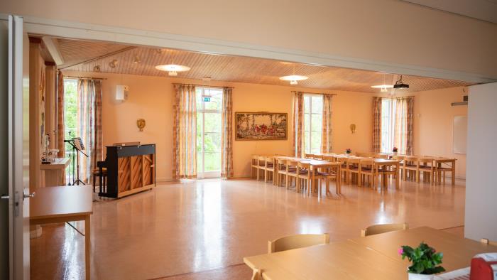 Vy över samlingssalen i Kimstads församlingshem. Till vänster står ett piano och till höger står långbord med stolar uppställda.