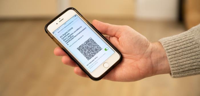 Mitt i bilden syns en smart telefon med ett covidpass med QR-kod framme. En hand håller i telefonen och kommer in från höger i bild.