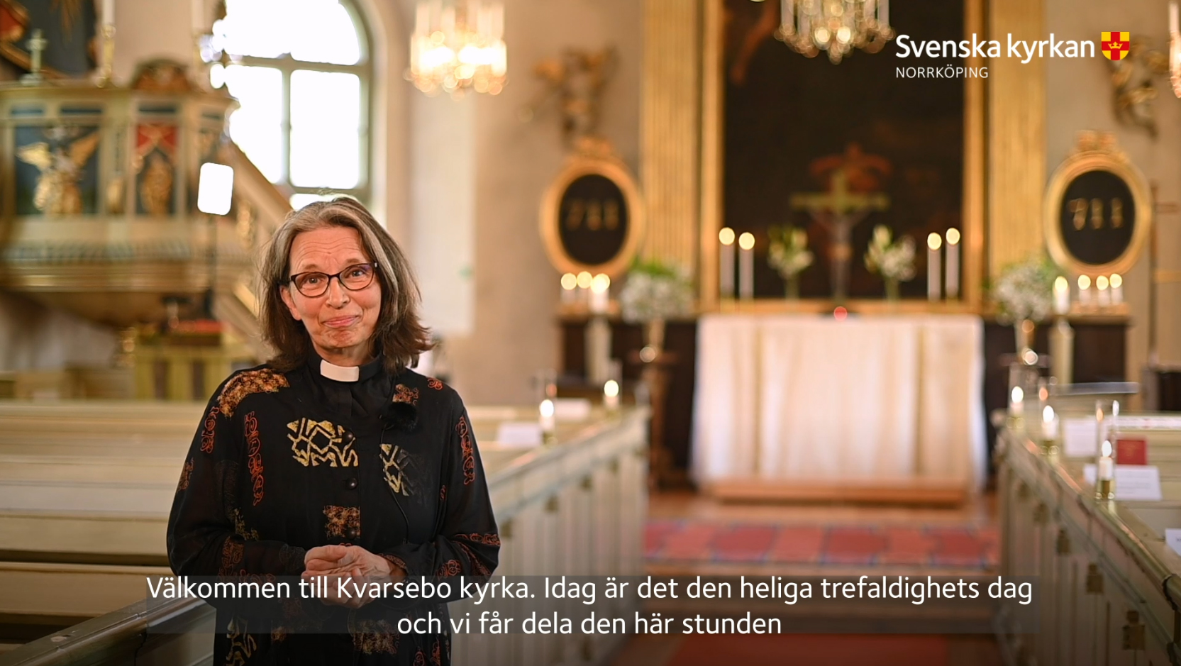 Präst Eva Strannelid står och hälsar välkommen i förgrunden, men en smyckad kyrka i oskärpa i bakgrunden.