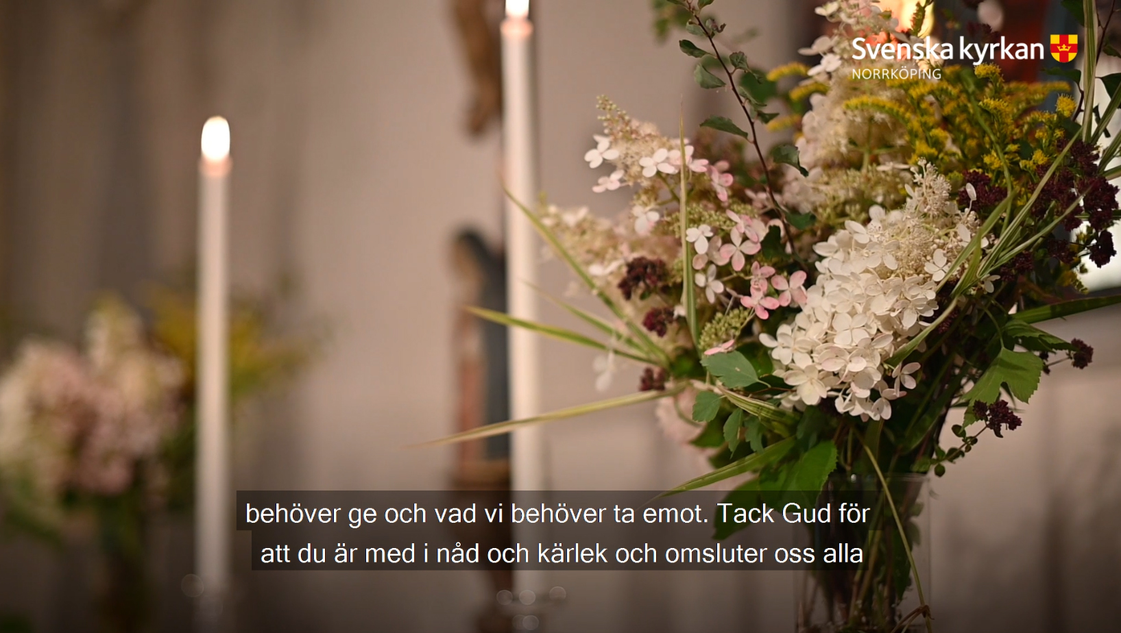 En vas med hortensia, murgöna och sommarblommor ses i förgrunden. I bakgrunden tända ljus.