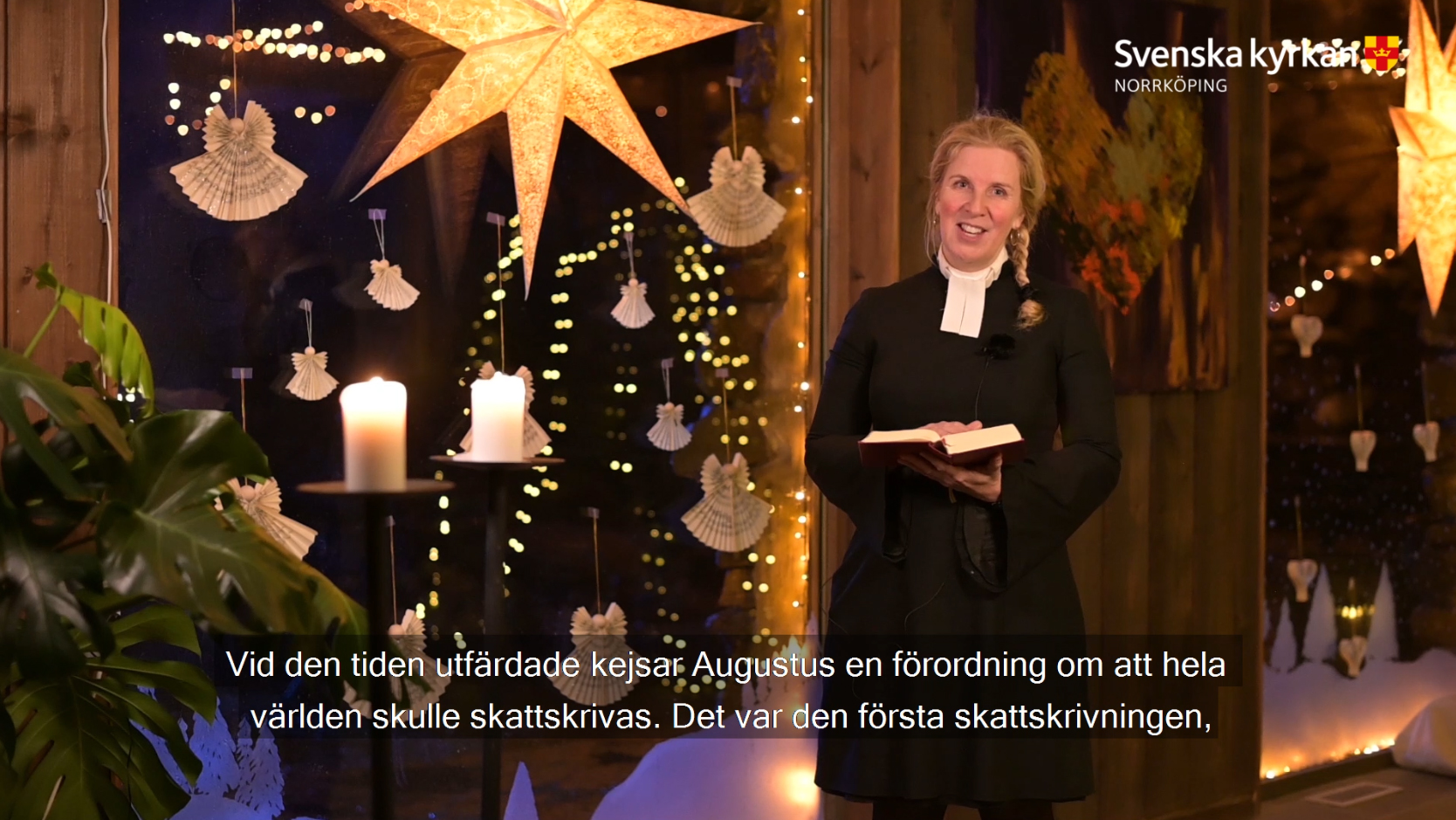 En bild av en kvinnlig präst som läser ur bibeln framför julsmyckat fönster.