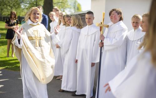 En präst hälsar på en konfirmand utanför en kyrka