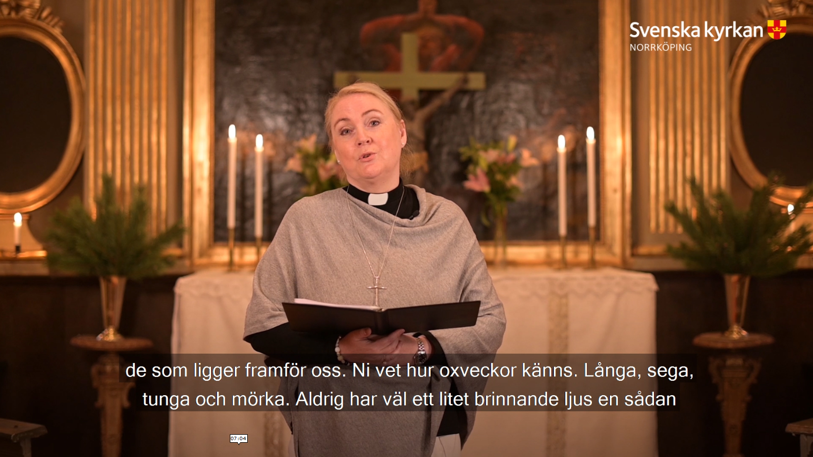 Präst Margareta Hagberg predikar framför ett altare smyckat med ljus och blommor. 