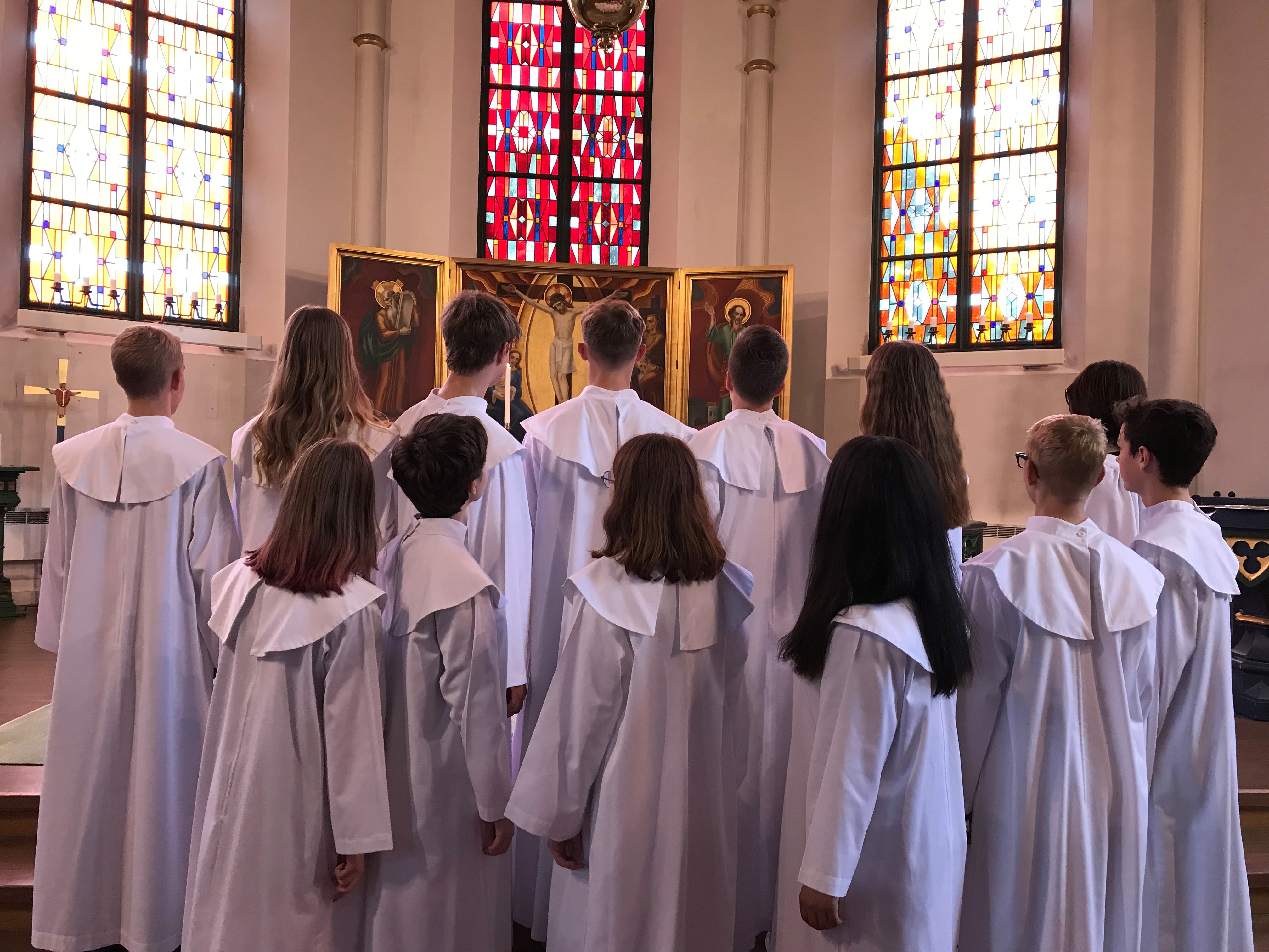 Konfirmandgrupp bakifrån i kåpor vid alter i Trollhättans kyrka