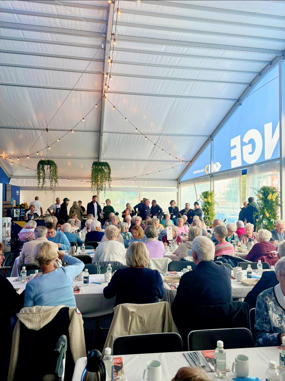 Bild från seniorträffen i eventtältet 2024 med glada penionärer vid långbord.