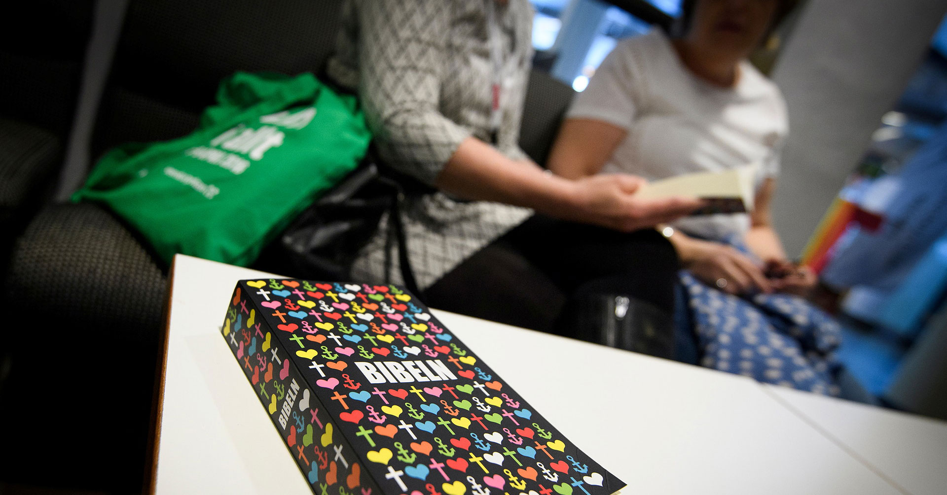 Bibel på ett bord, två personer sitter i bakgrunden