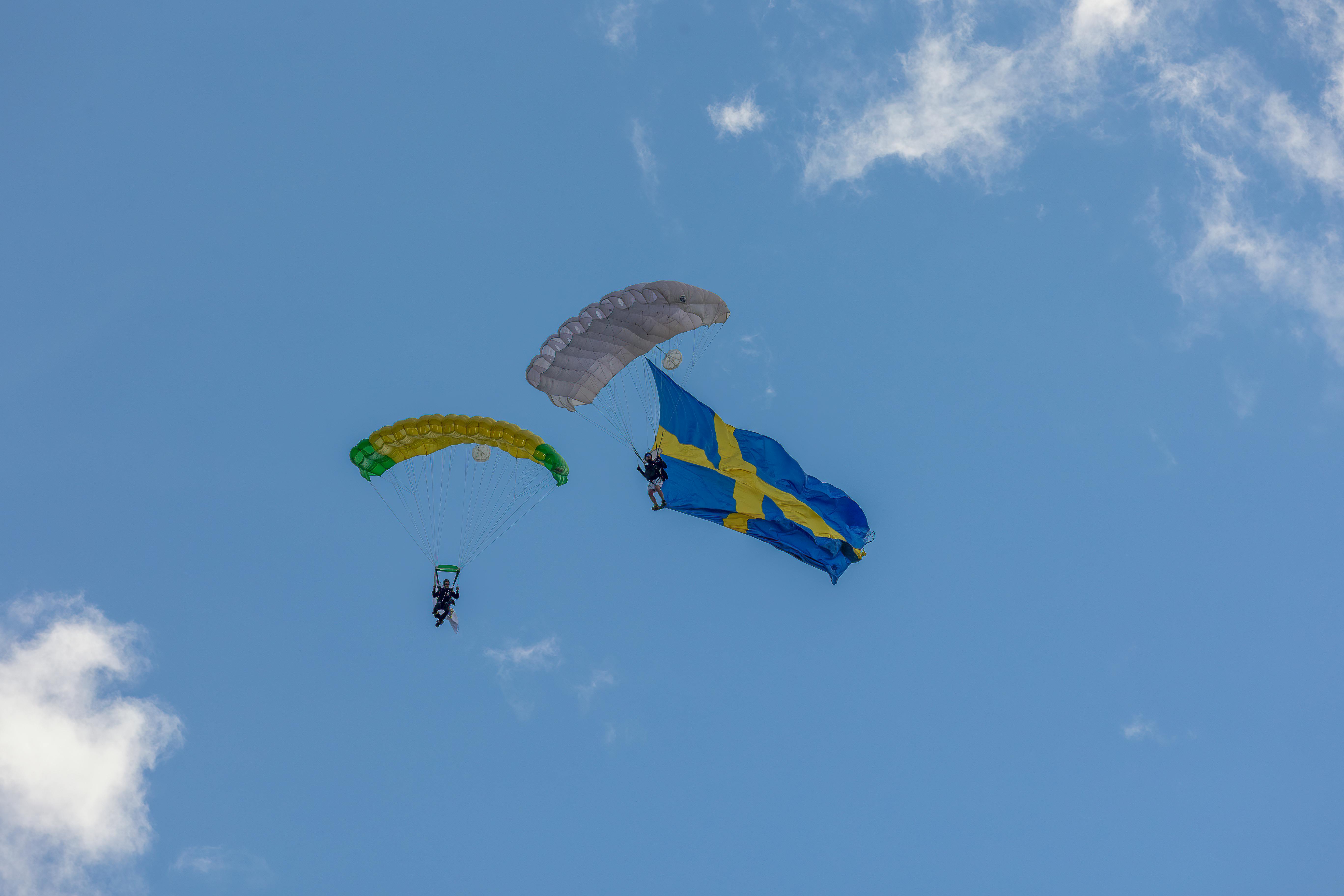 Två fallskärmshoppare i luften visar upp en svenska flagga.