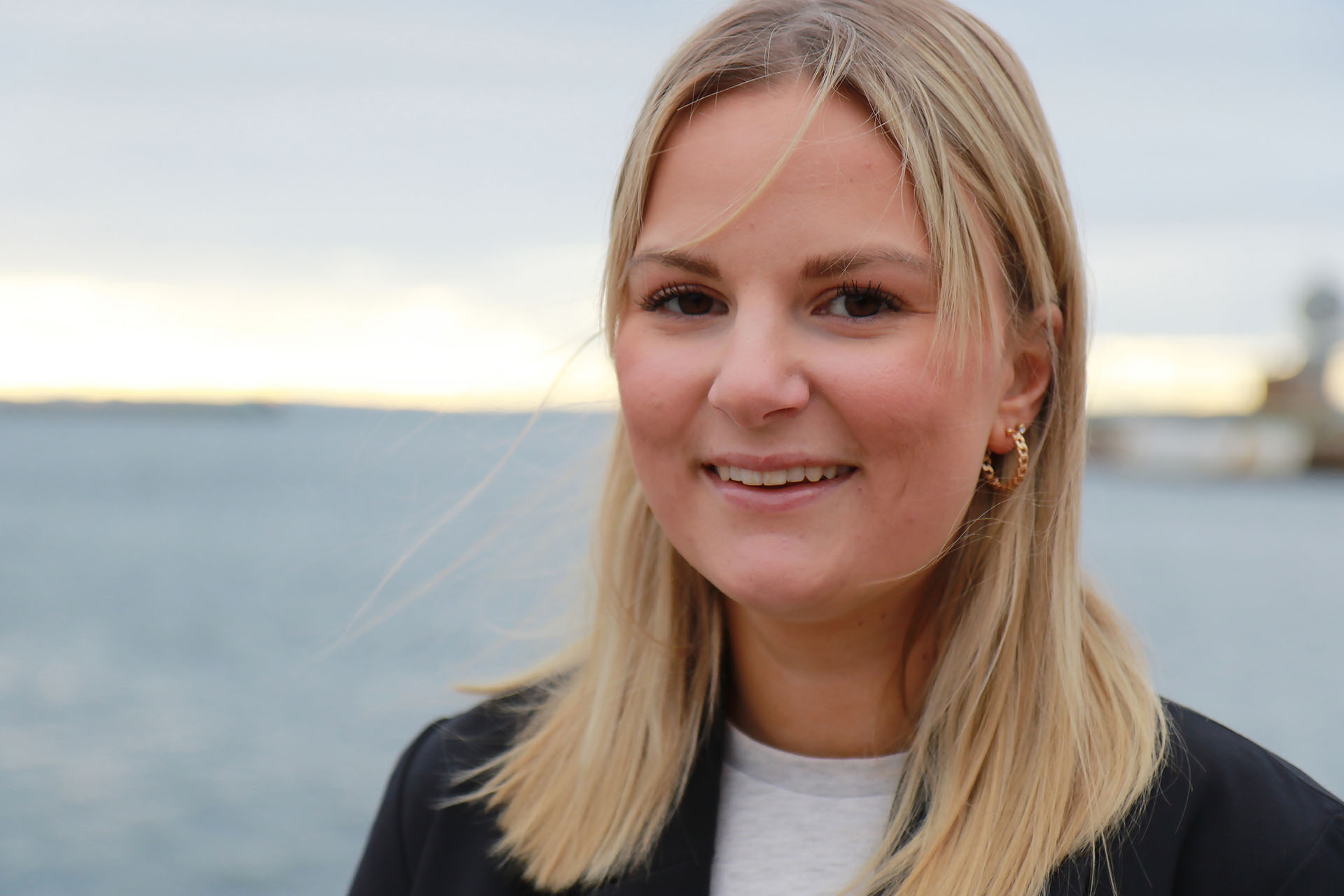En närbild på en kvinna i blont axellångt hår. I bakgrunden syns havet.