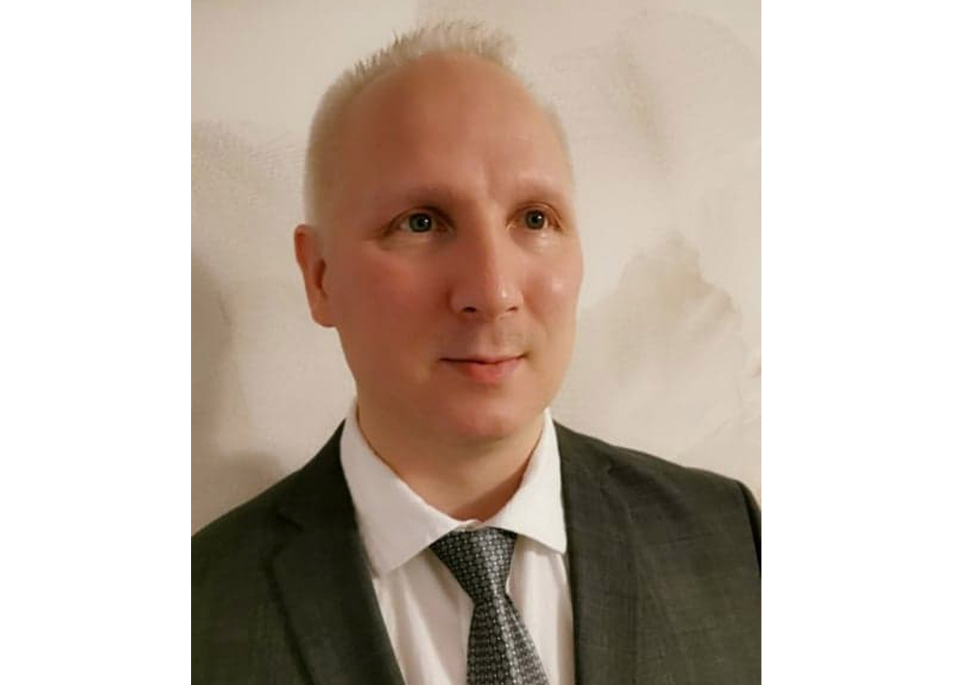 Närbild på en man med kort ljust hår, klädd i mörk kostym och slips.