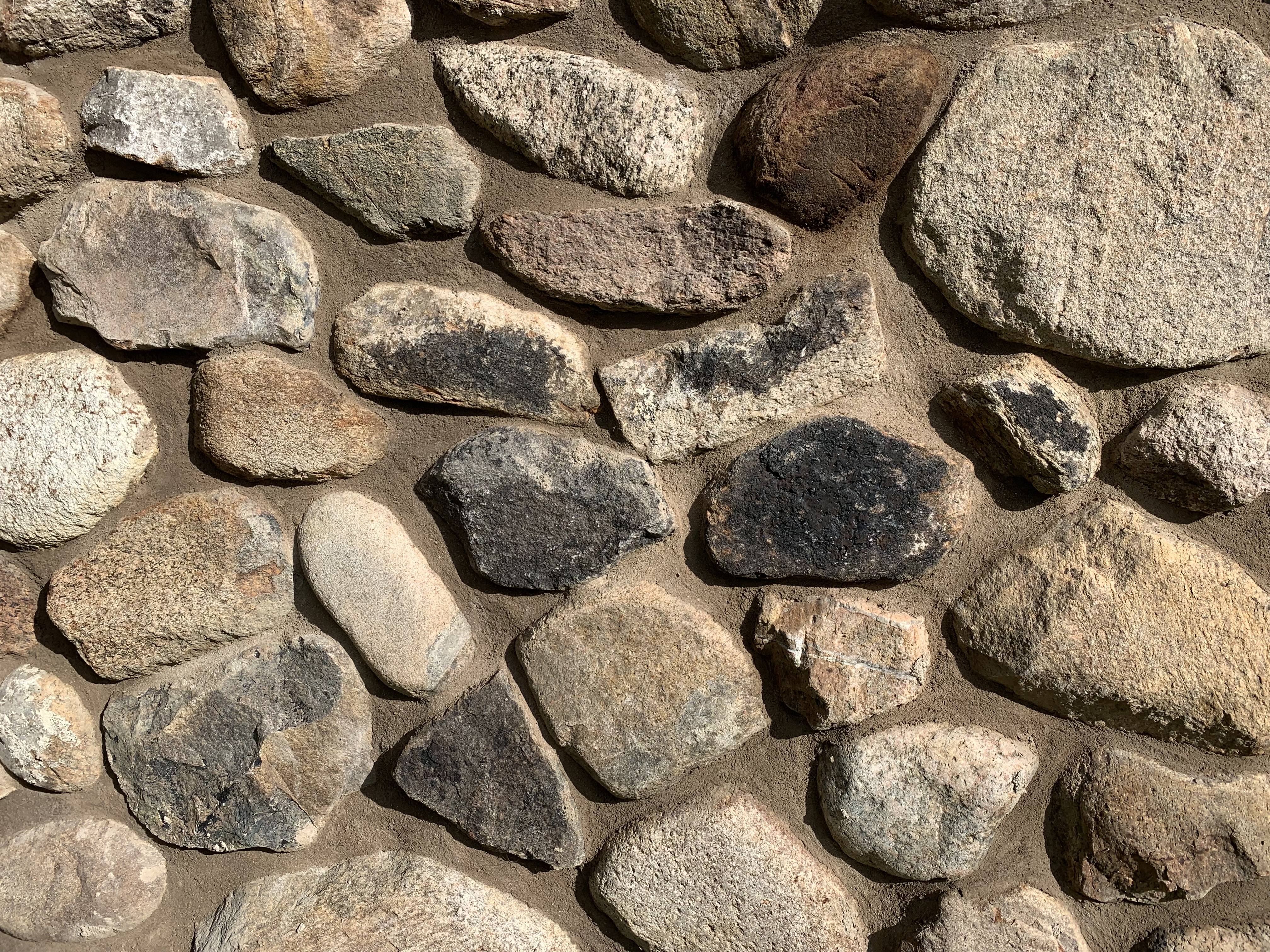 Bild av en mur bygd av naturstenar i olika färger och former 