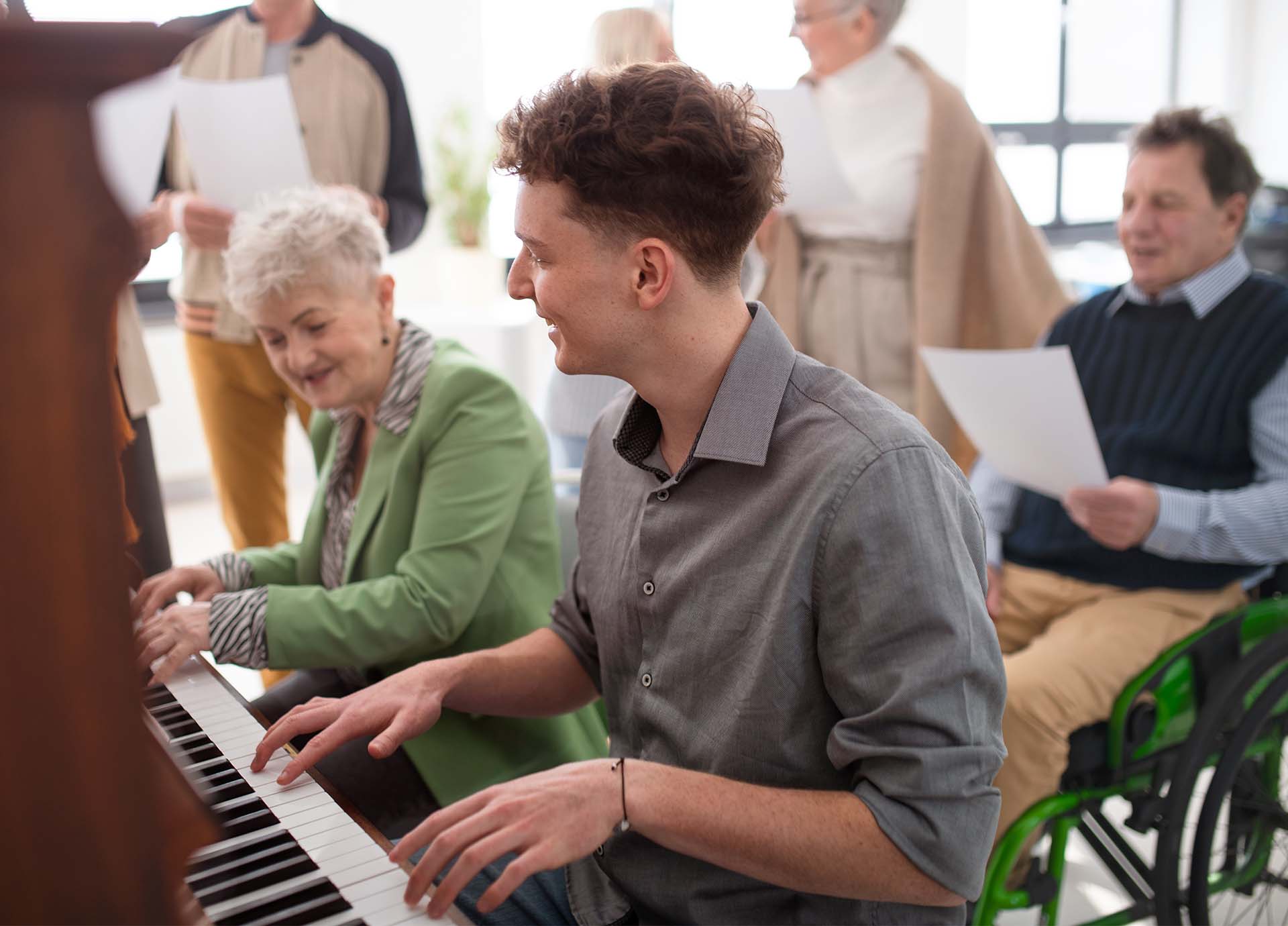 En ung man och en äldre kvinna ler och spelar piano tillsammans