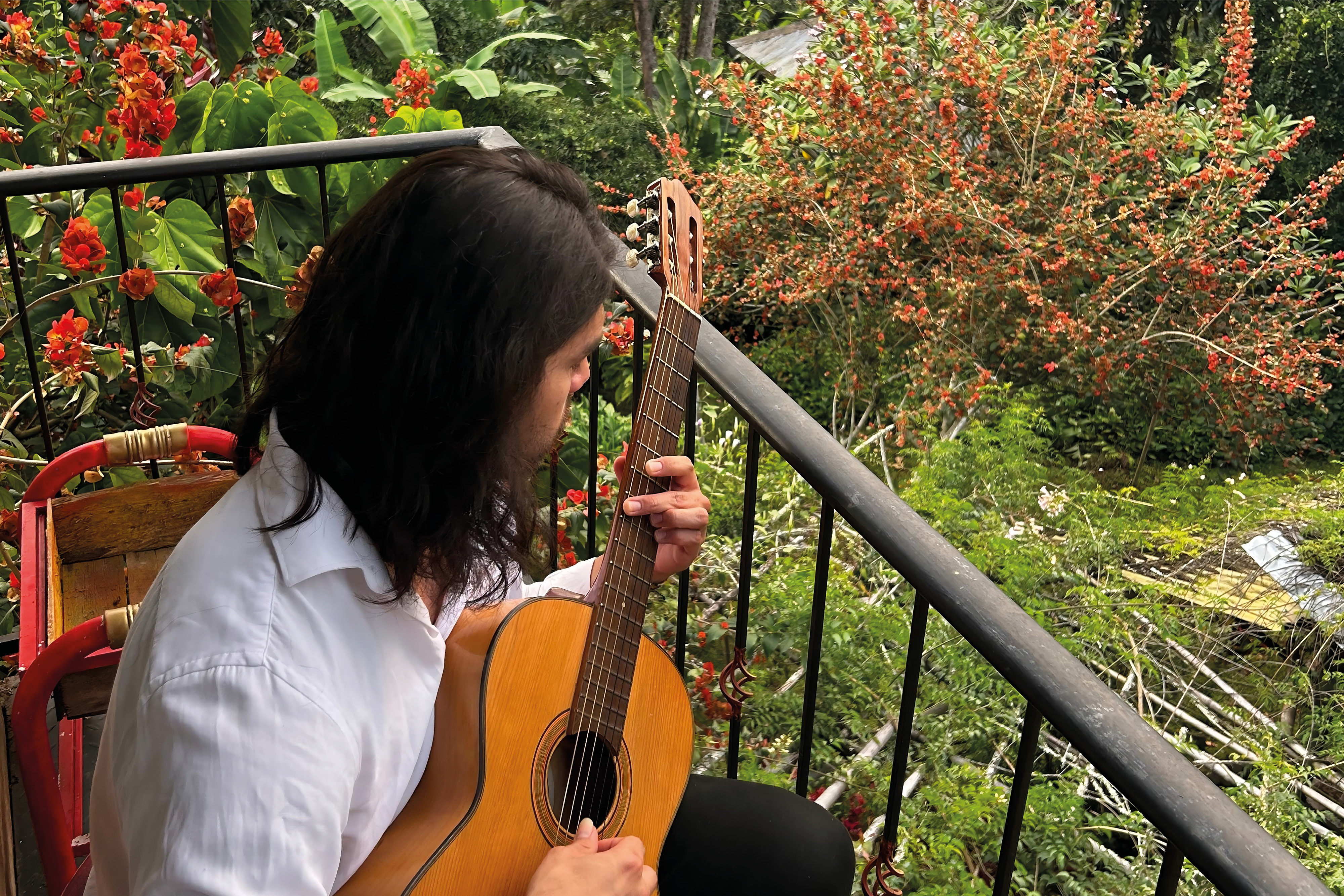 Person spelar gitarr på en balkong omgiven av grönskande natur