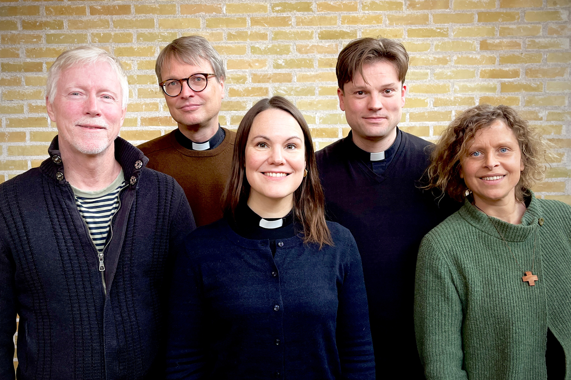 Fem personer står mot en gul tegelvägg. 