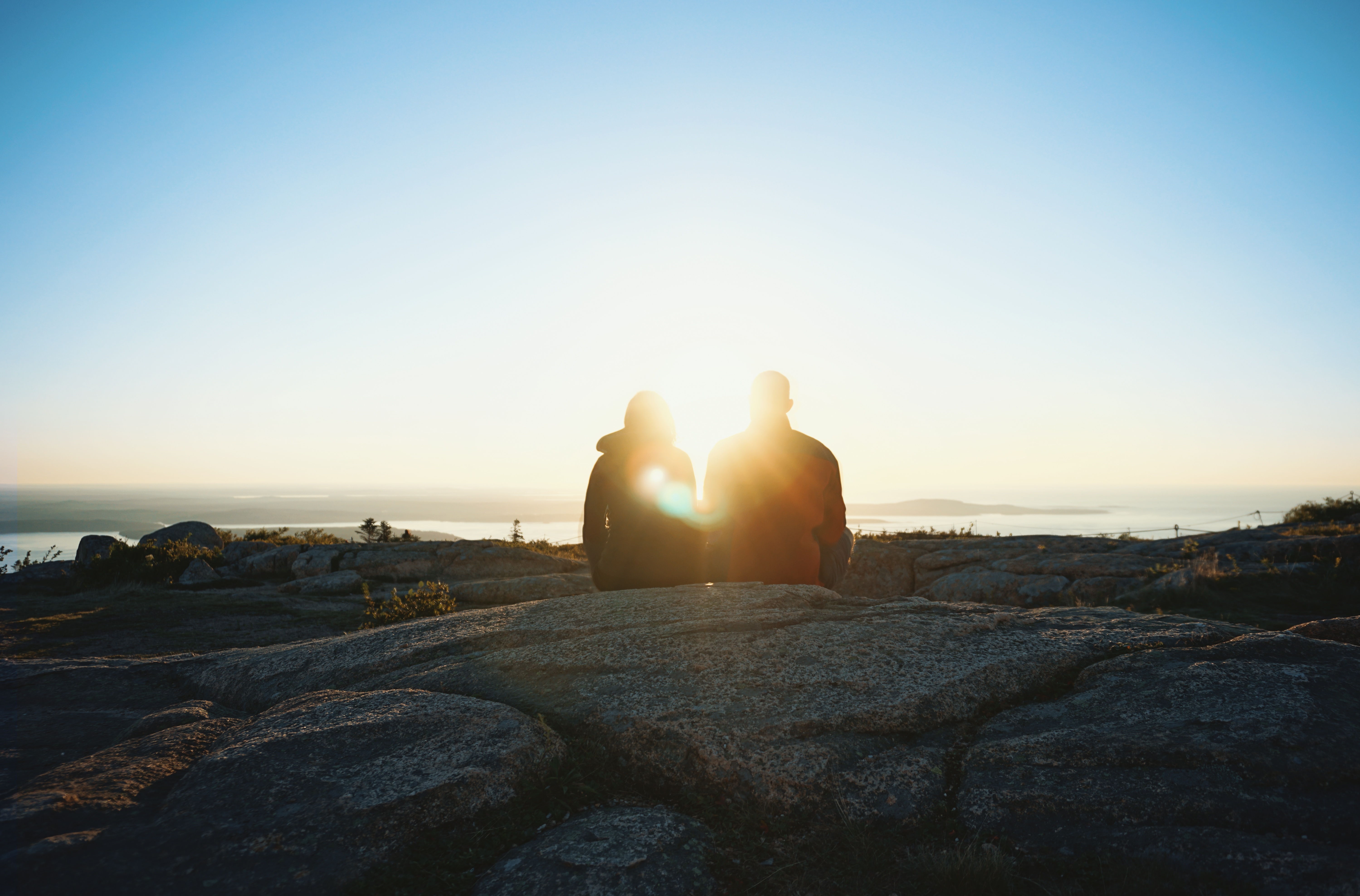 Ett par sitter på en klippa i motljus i solnedgång.