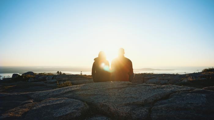 Ett par sitter på en klippa i motljus i solnedgång.