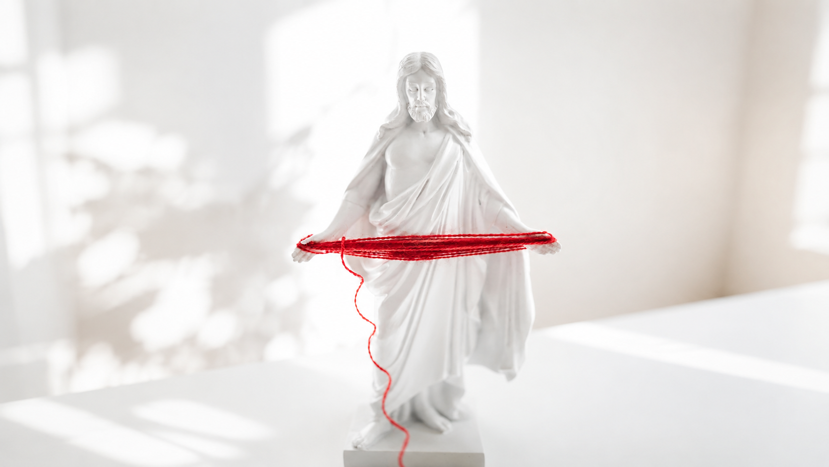 En vit Jesus-staty som håller rött garn