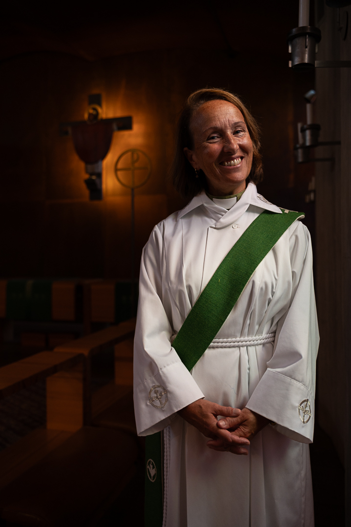 En diakon klädd i vit dräkt och grönt band. I bakgrunden skymtas ett upplyst kors.