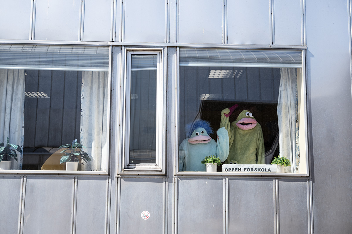 Två personer i monsterdräkter skymtas genom ett fönster. Texten öppen förskola syns på en skylt.
