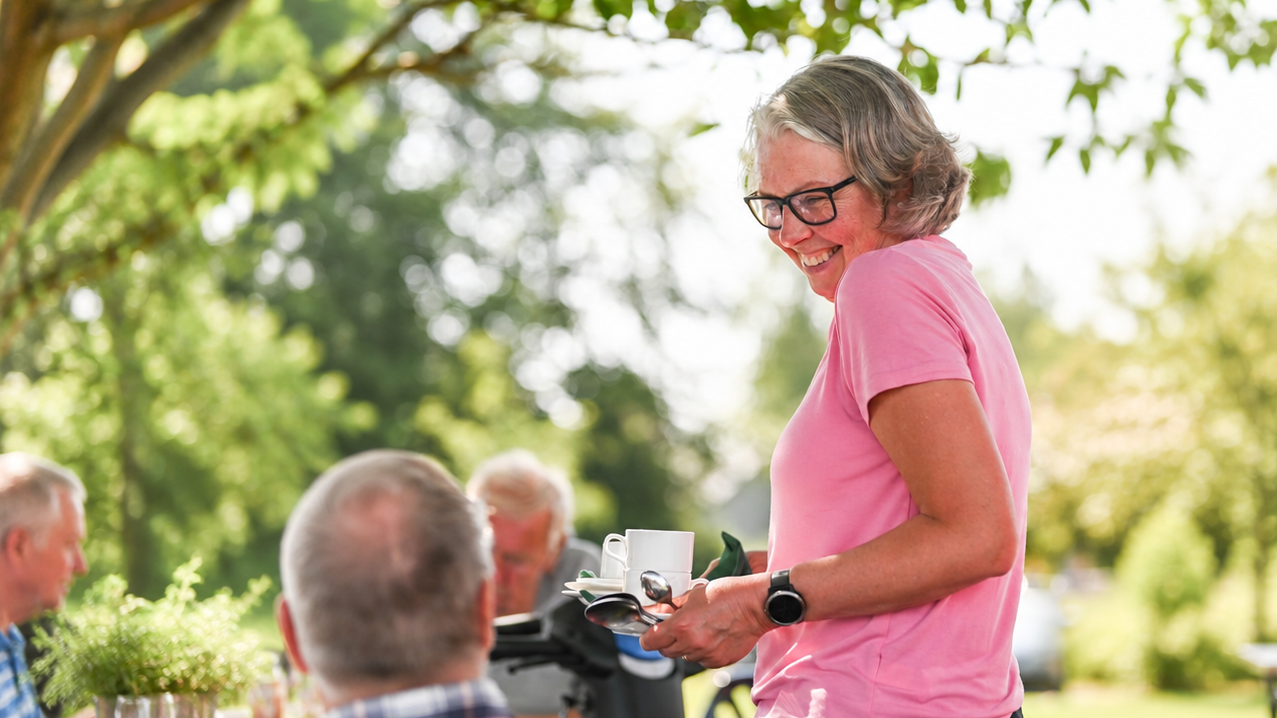 En kvinna i rosa t-shirt som håller i en kaffekopp och pratar med en man som syns bakifrån.