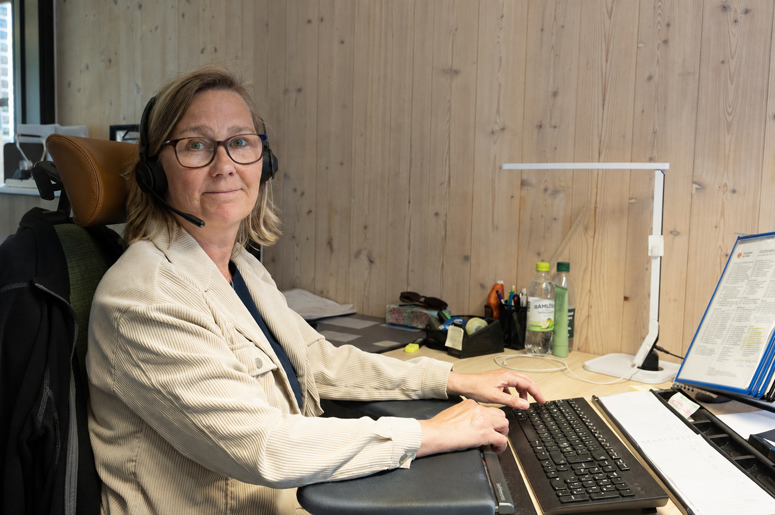 En kvinna sitter på ett kontor ed headset redo att svara i telefon