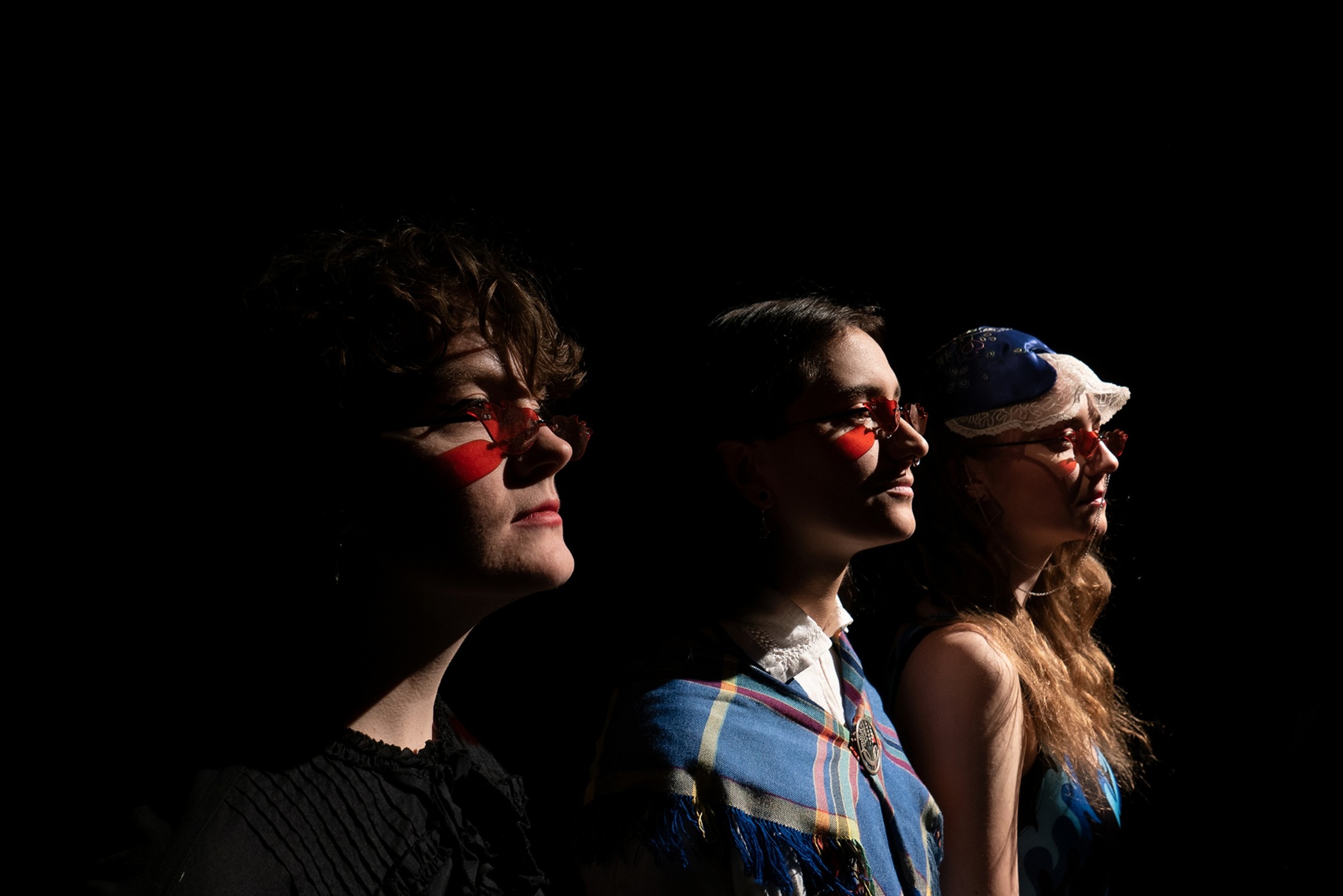 Tre personer tittar åt höger i profil. De är målade och koncentrerade.