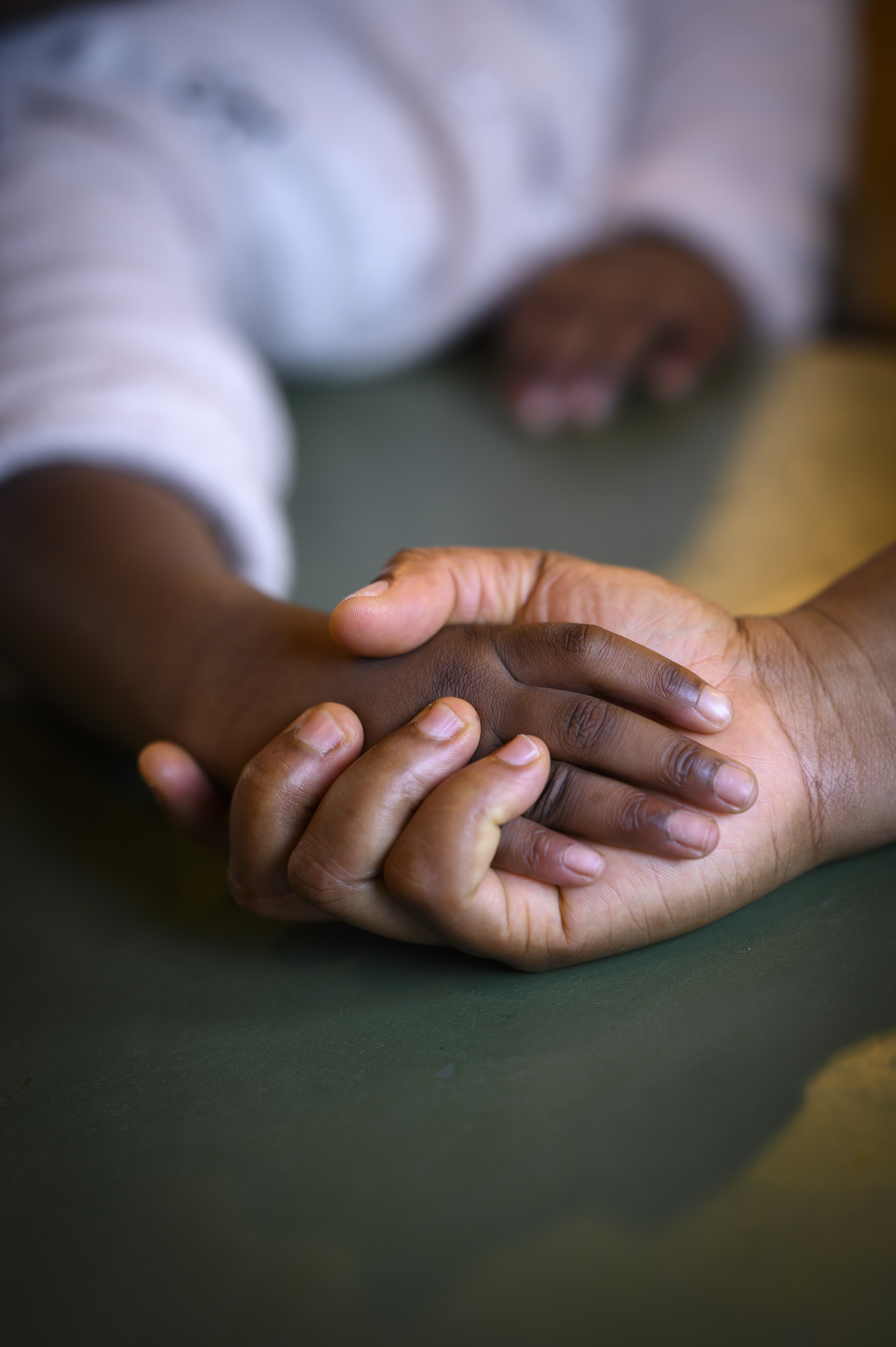 En barnhand som håller i en vuxenhand. Händerna ligger på ett bord.