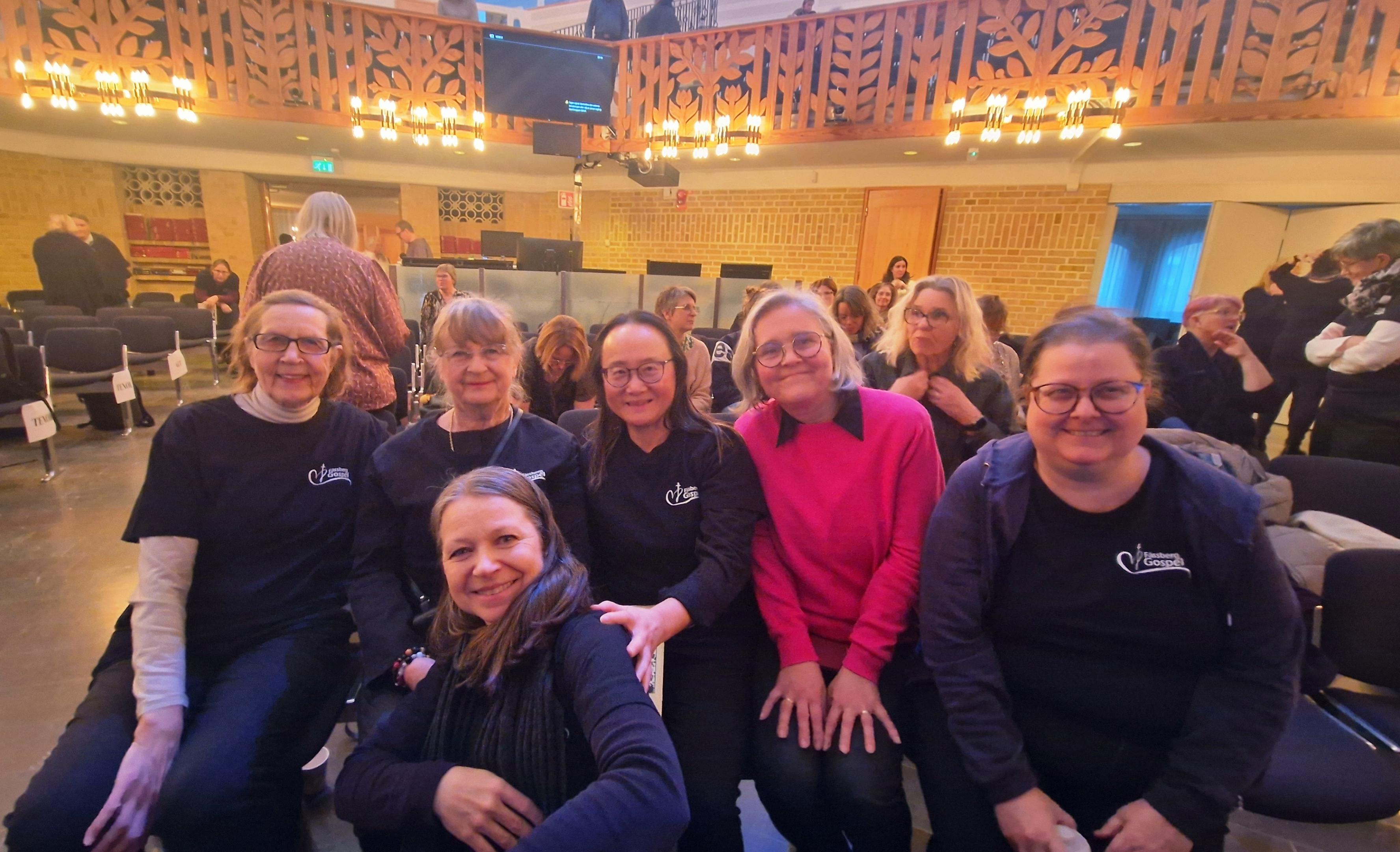 Sju glada kvinnor tittar in i kameran. De sitter i en kyrka.