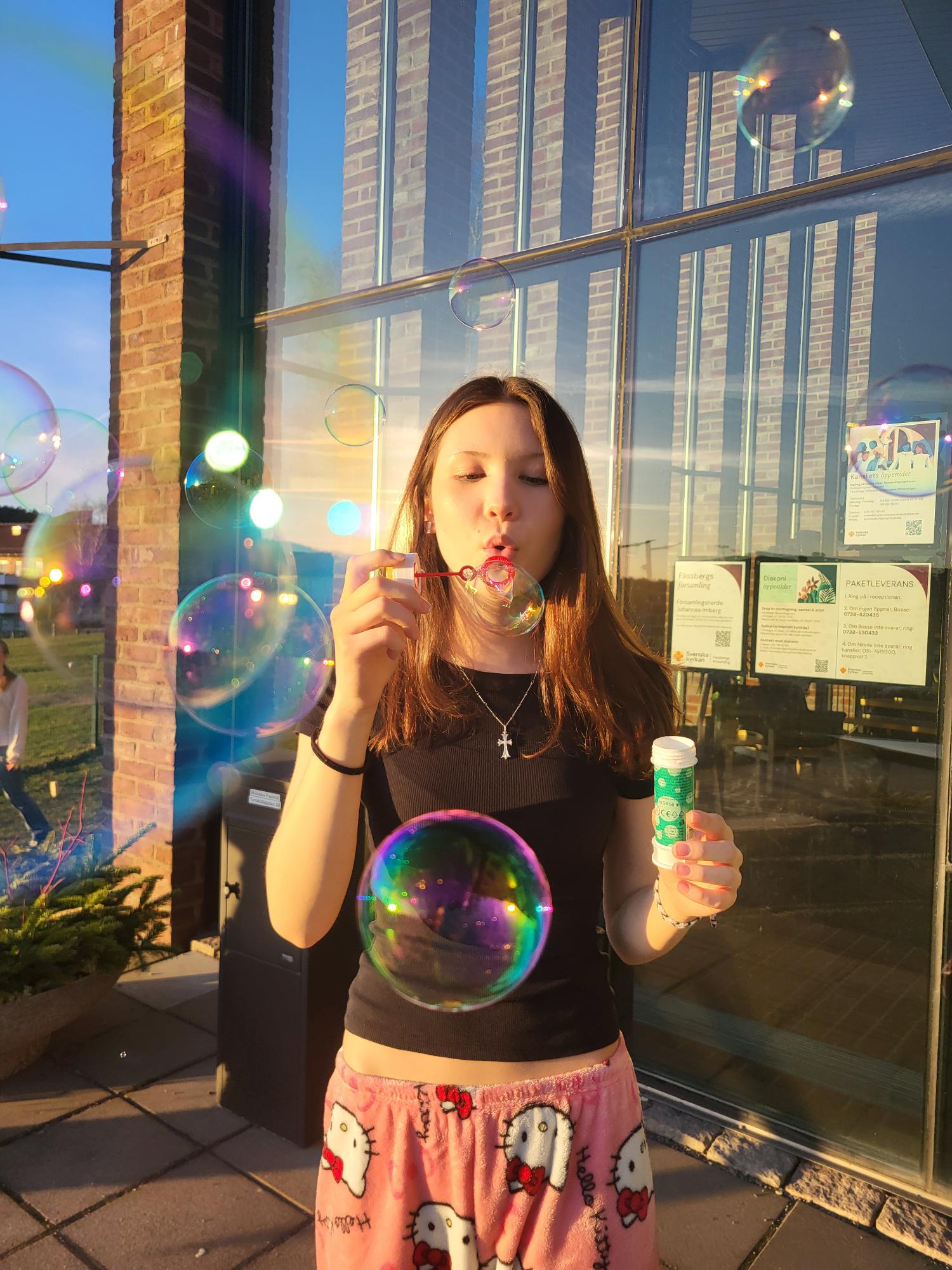 En flicka står i solen och blåser stora såpbubblor.