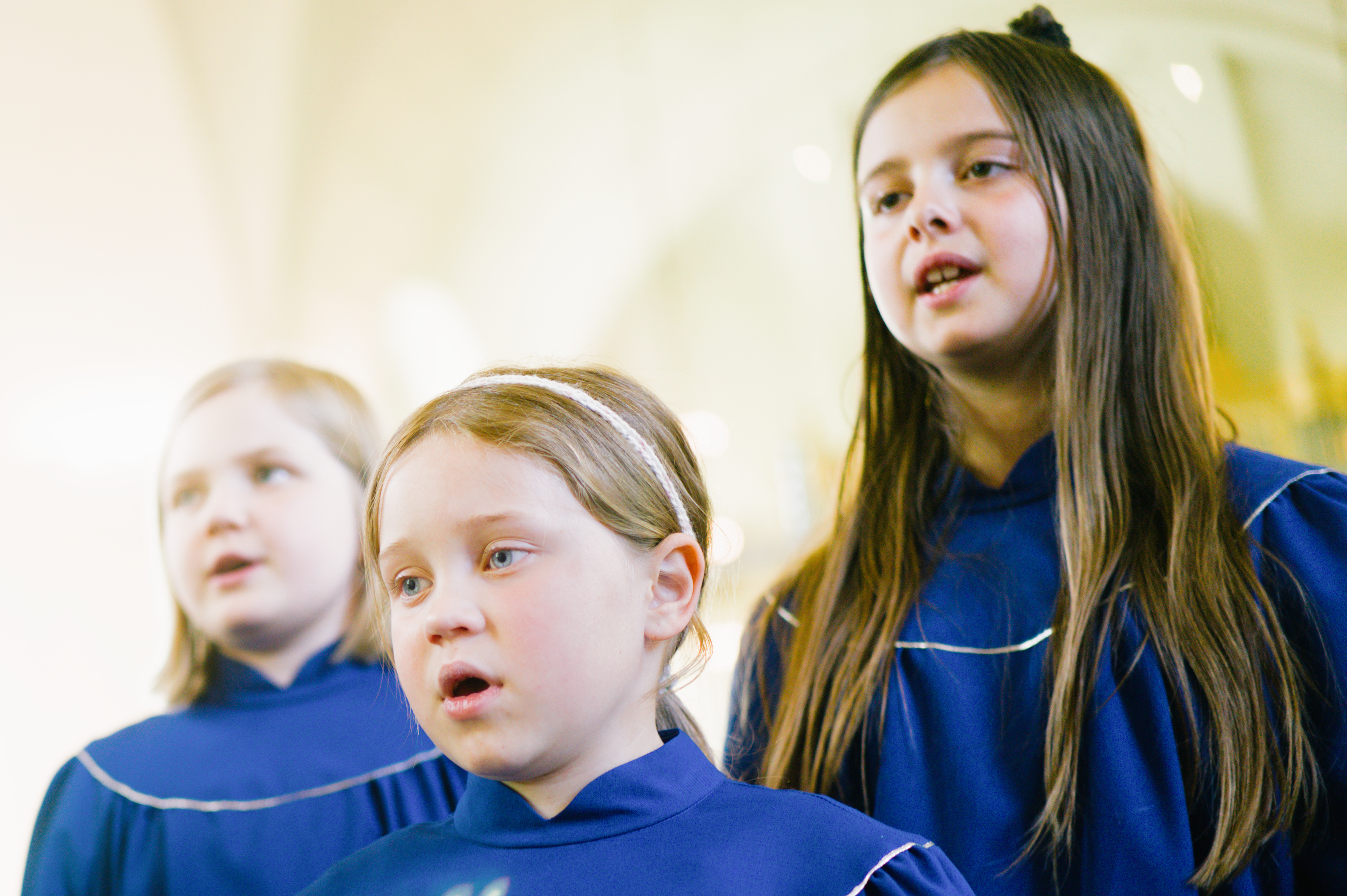 Närbild på tre flickor i två kåpor som sjunger i kyrka