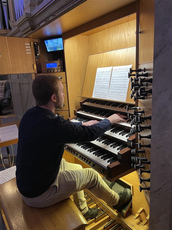 En ung man med mörk tröja och beige byxor sitter och spelar orgel.