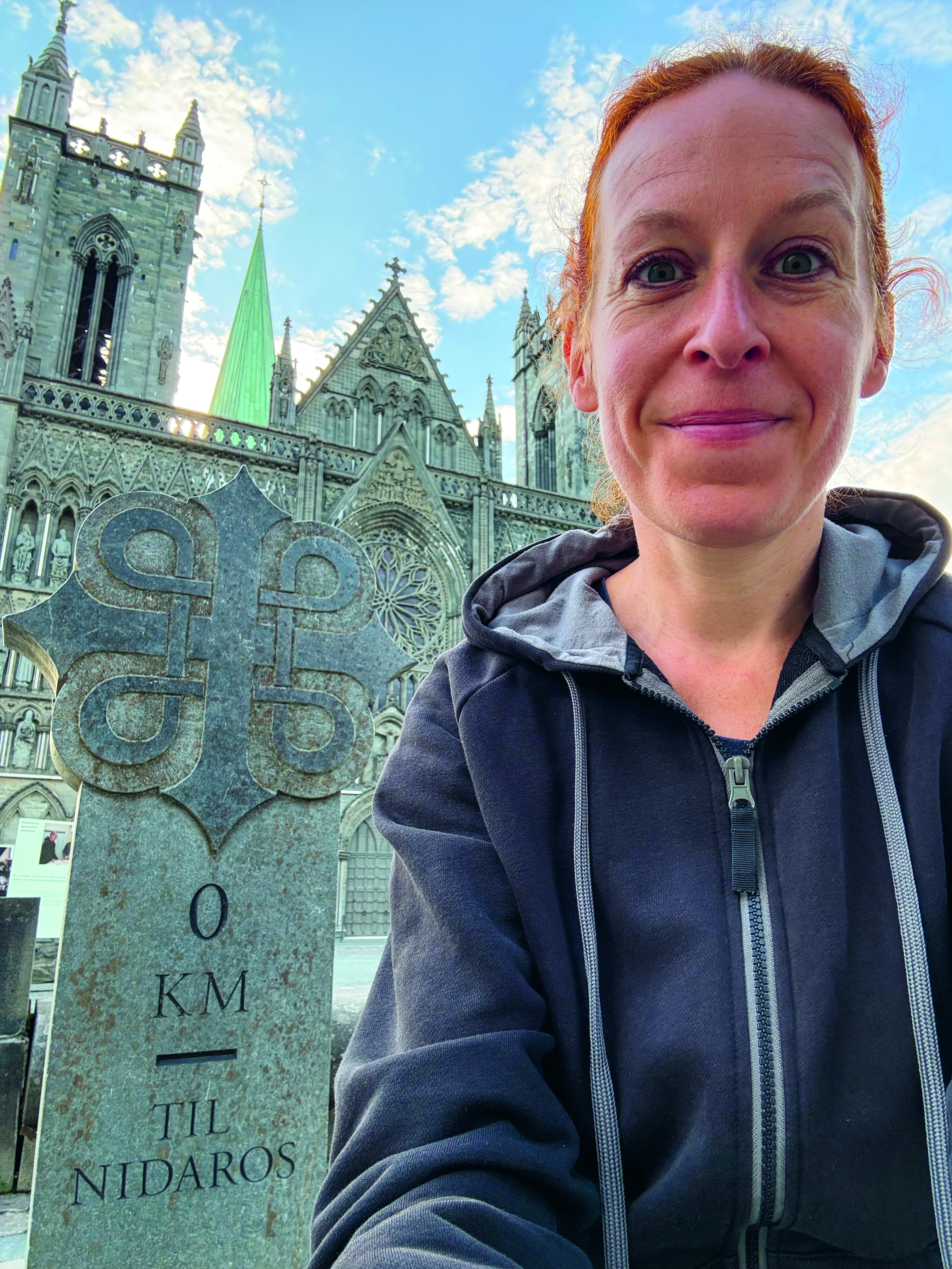 Kvinna i huvtröja och uppsatt hår står framför en stor kyrka.