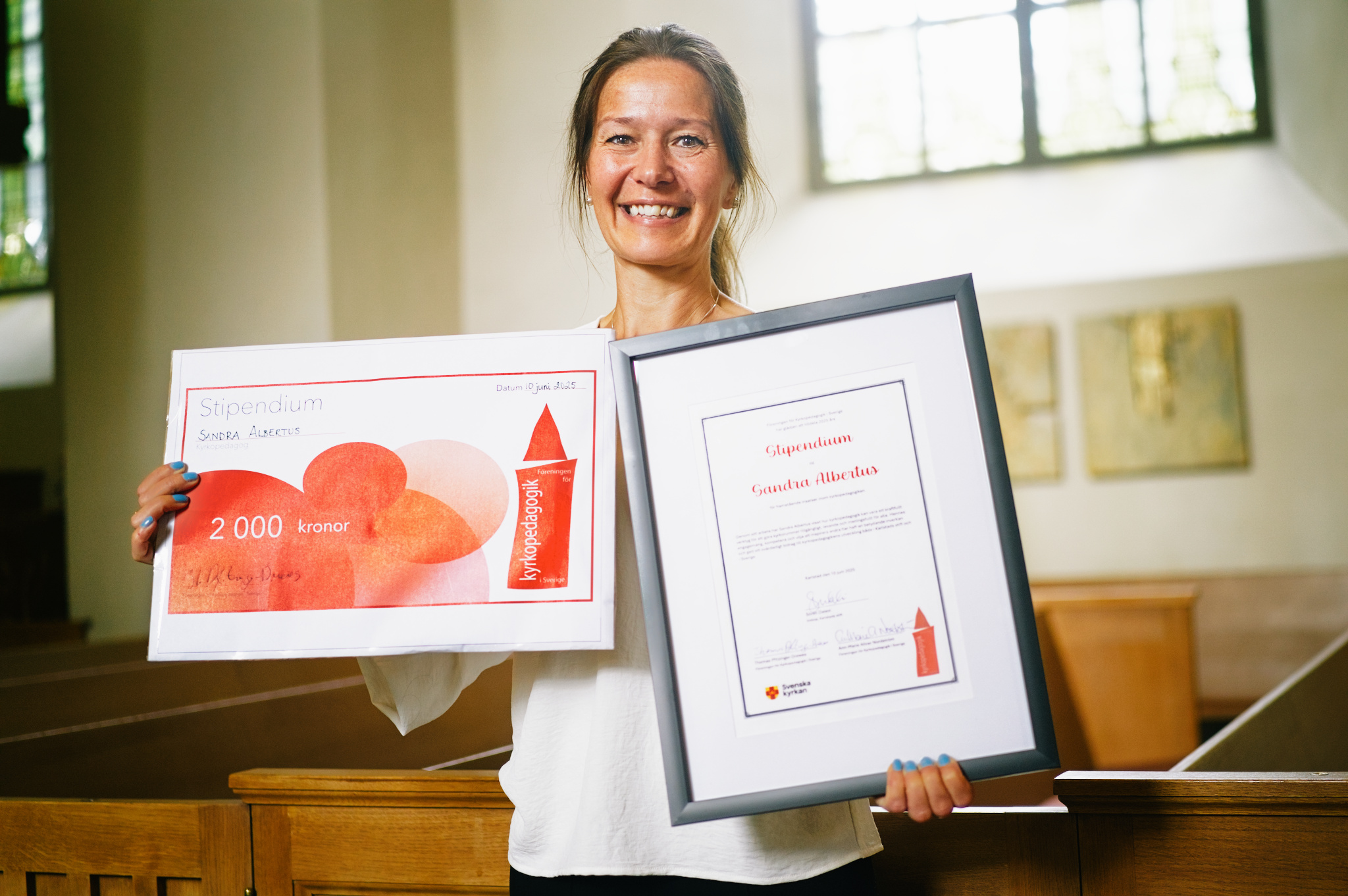 Kvinna i kyrka håller stipendie i sina händer