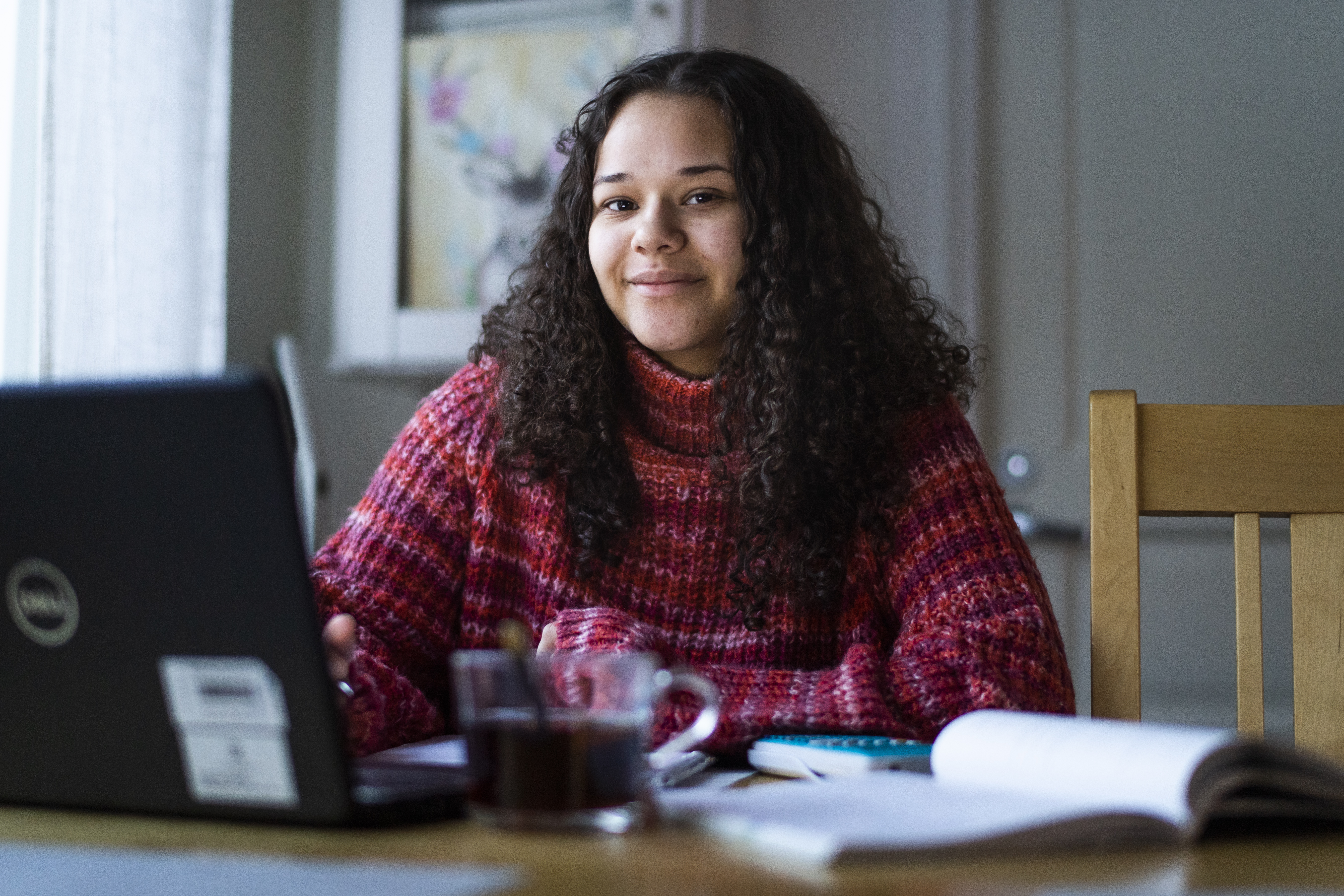 Ung kvinna med mörkt långt hår sitter framför en datorskärm. I förgrunden syns en kopp kaffe