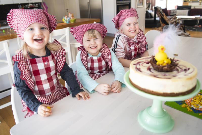 Tre flickor i sjalett framför en nybakad cheesecake. 