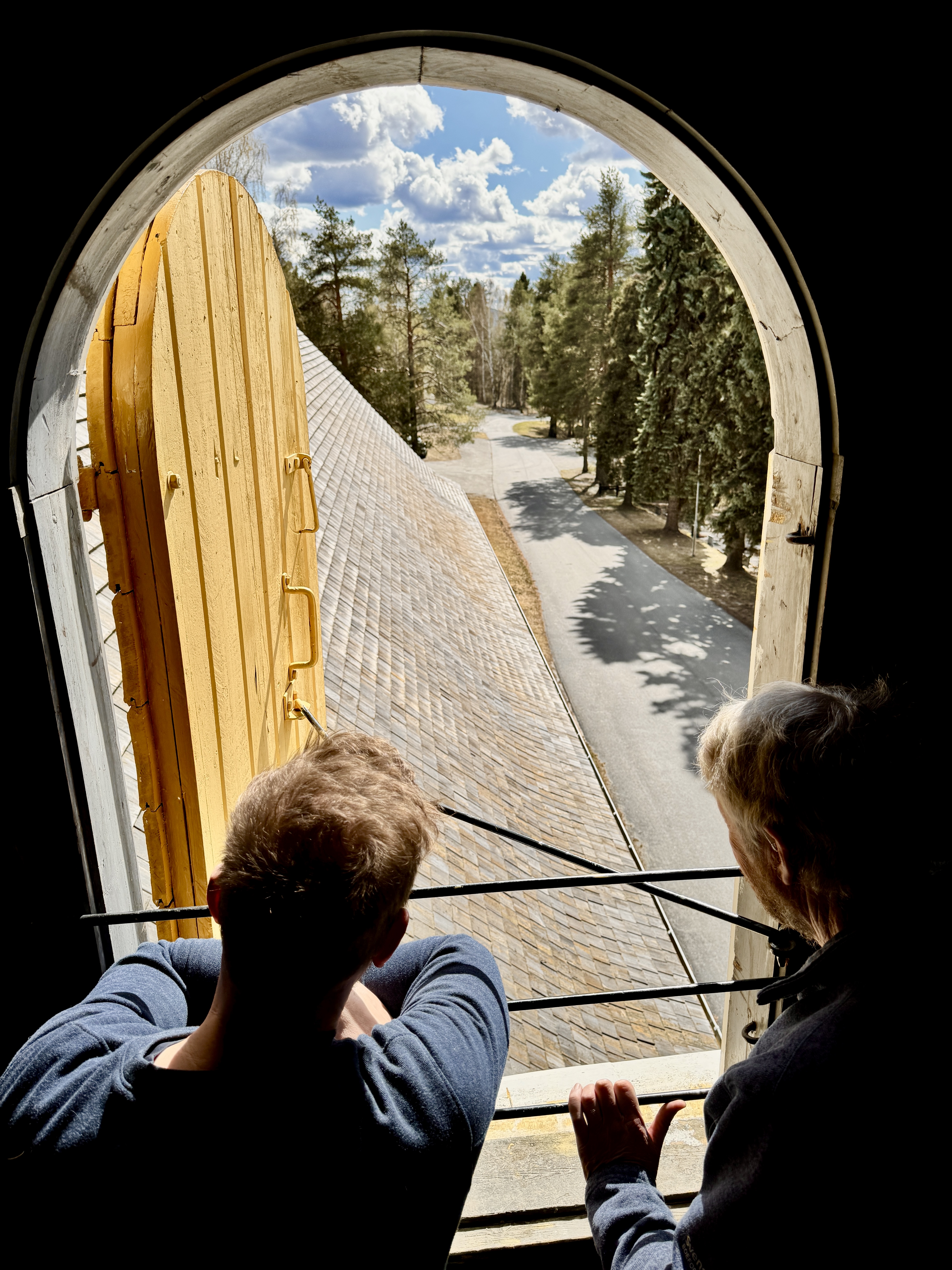 En glimt av omgivningarna från kyrktornet, där vägen, träden och kyrkans tak breder ut sig under en klar himmel.