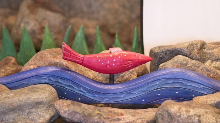 En röd fisk utskuren i trä simmar vid foten av konstverket Björkens visa. 