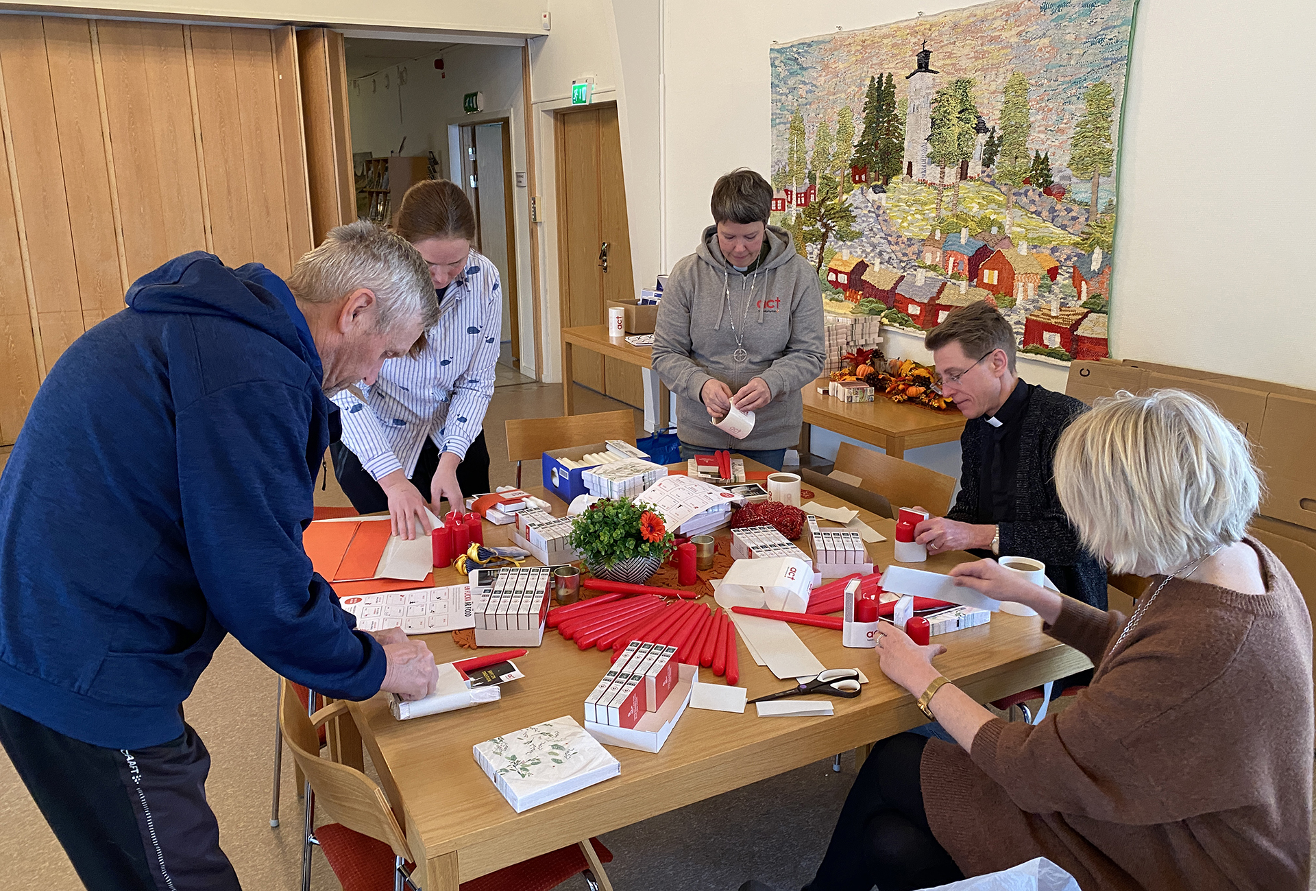 Tre kvinnor och två män är samlade kring ett bord för att pyssla ihop julgåvor. 