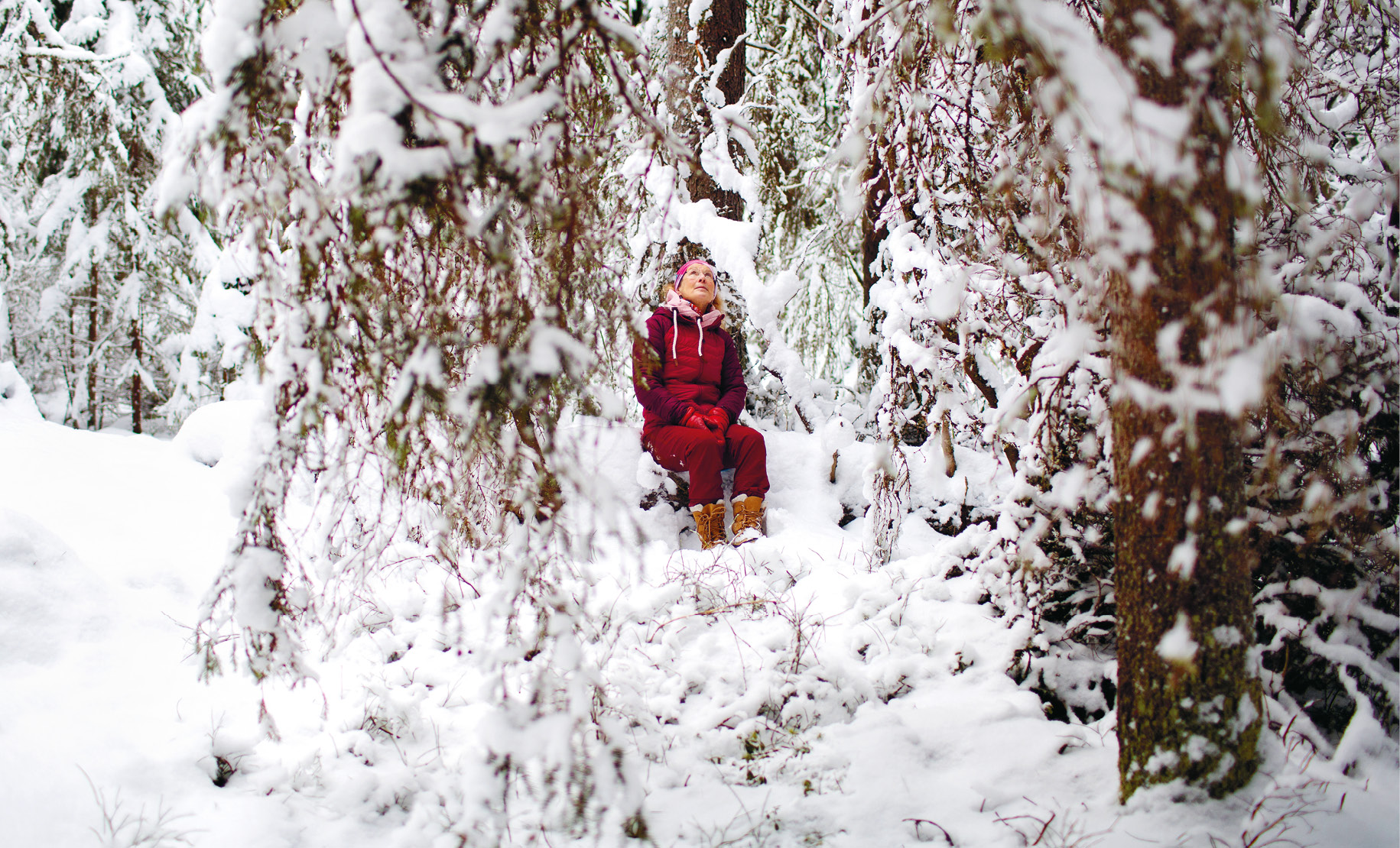 Kvinna i röda kläder sitter mitt i snöig skog.