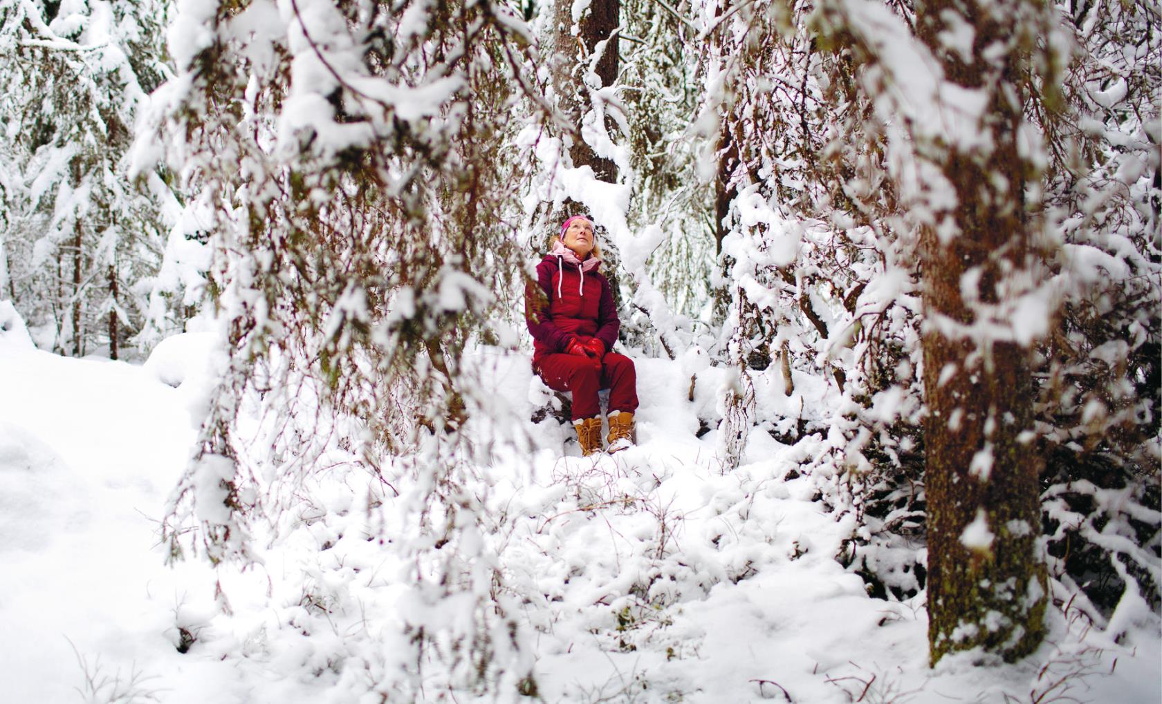 Kvinna i röda kläder sitter mitt i snöig skog.