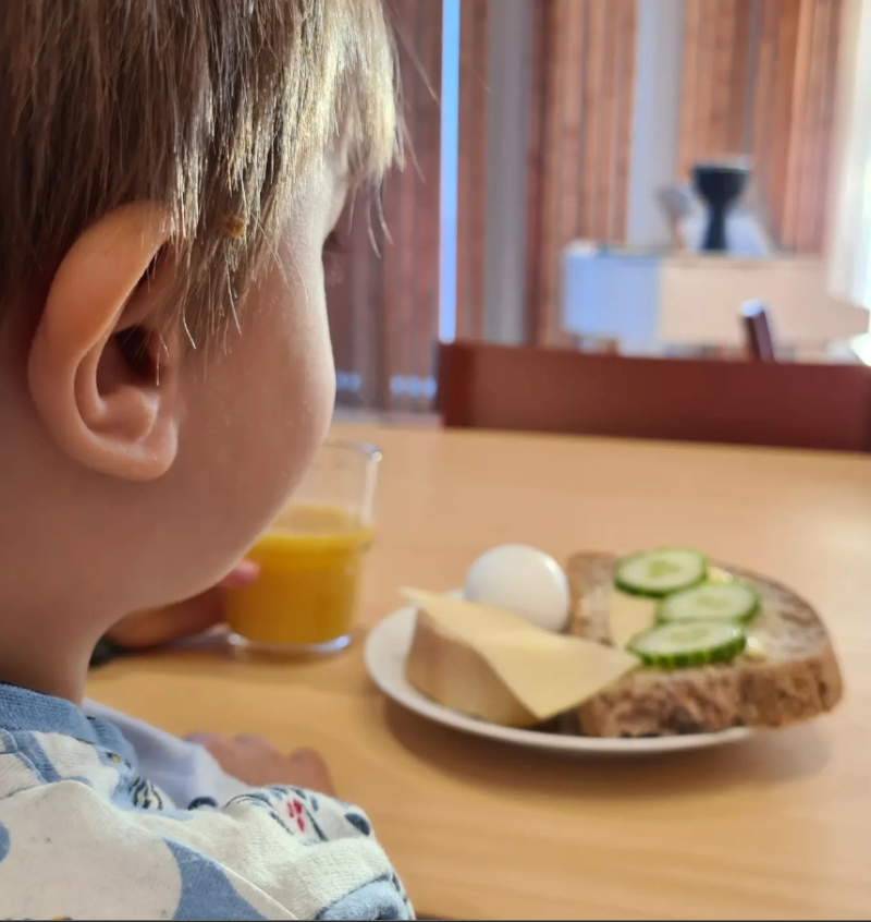 Litet barn äter frukost, ostsmörgås med gurka, ägg och ett glas juice. 